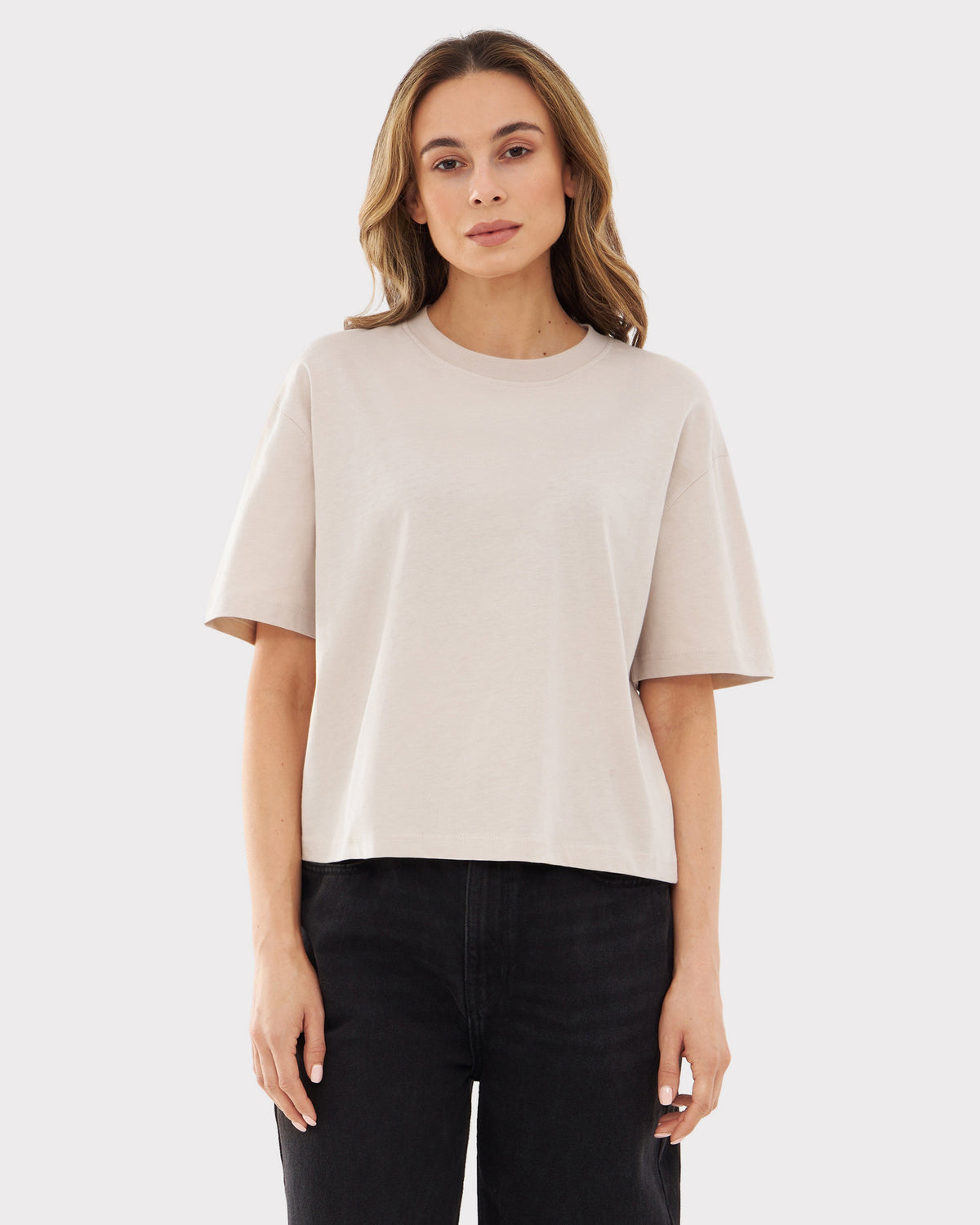 Frau mit beige Cropped T-Shirt 'Zoey' und schwarzen Hosen, stehend vor weißem Hintergrund