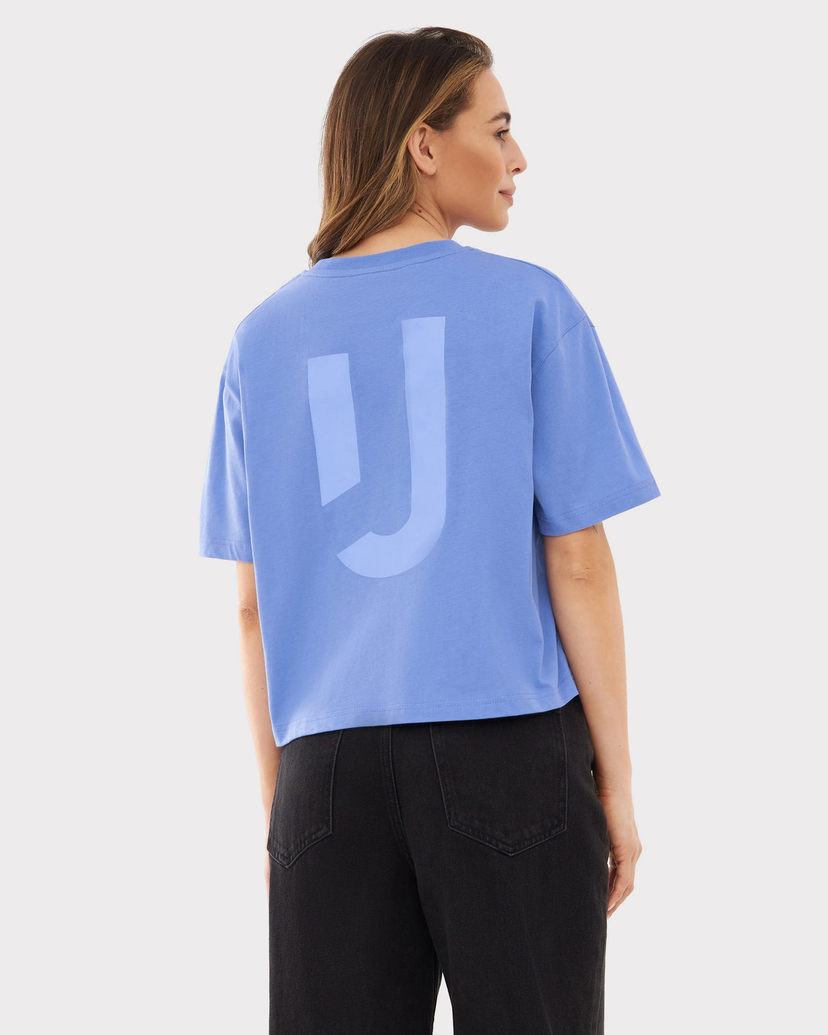 Frau trägt oversized cropped T-Shirt 'Zoey JU' in Blau mit lila Print vom Rücken