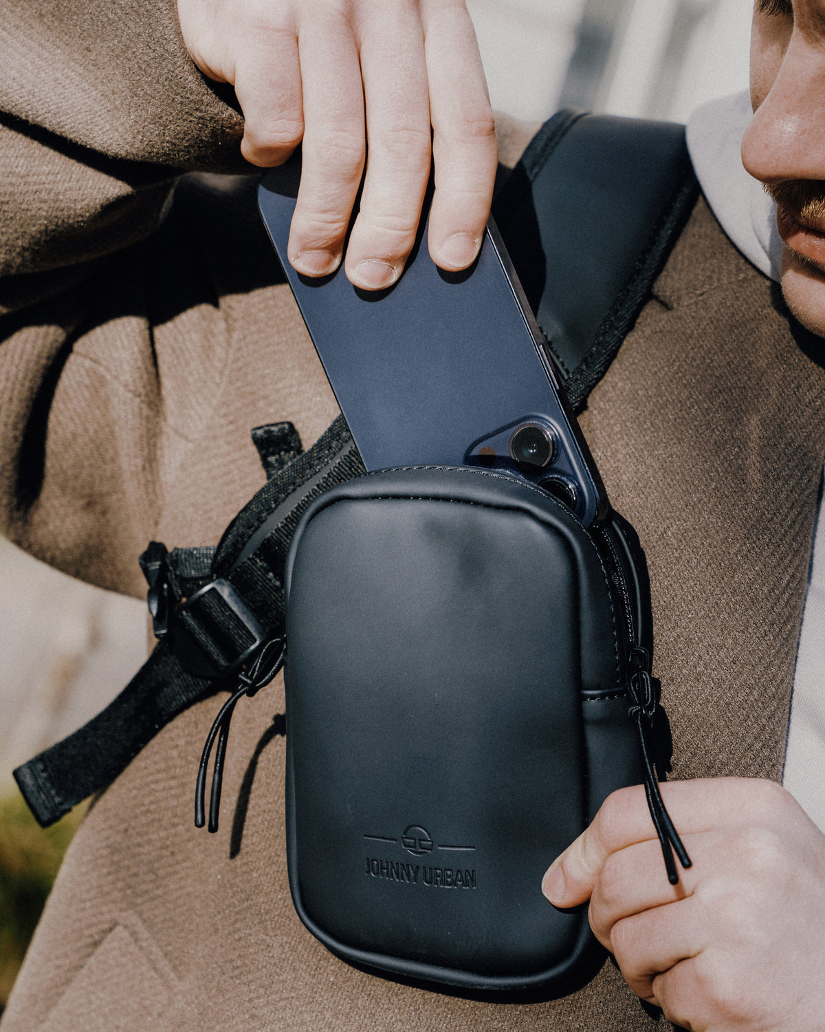 Person steckt ein Smartphone in das schwarze Front Pack 'Toby' von Johnny Urban