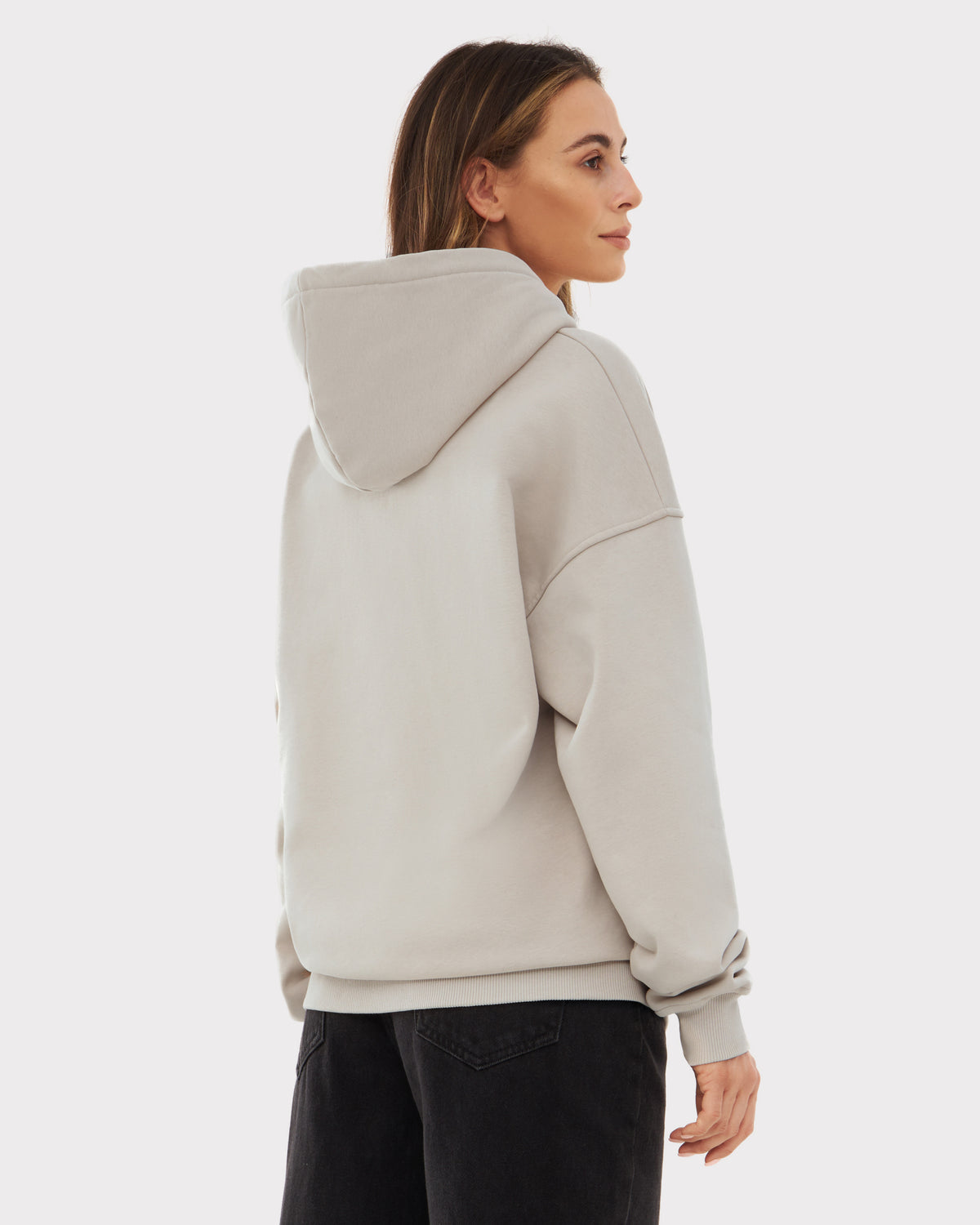 Frau trägt oversized Hoodie 'Cody' in hellem Beige, Rückansicht, kombiniert mit hellblauen Jeans