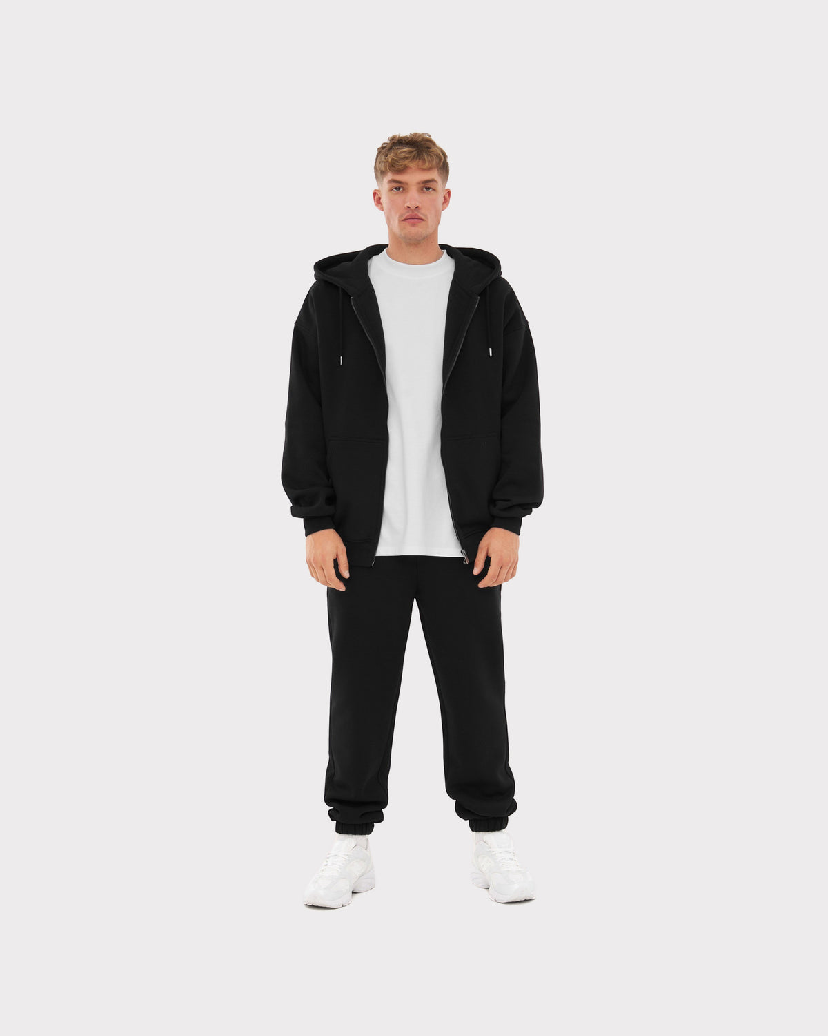 Mann trägt schwarze Jogginghose 'Owen' von Johnny Urban mit weißem T-Shirt, schwarzer Zip-Hoodie und weißen Sneakern