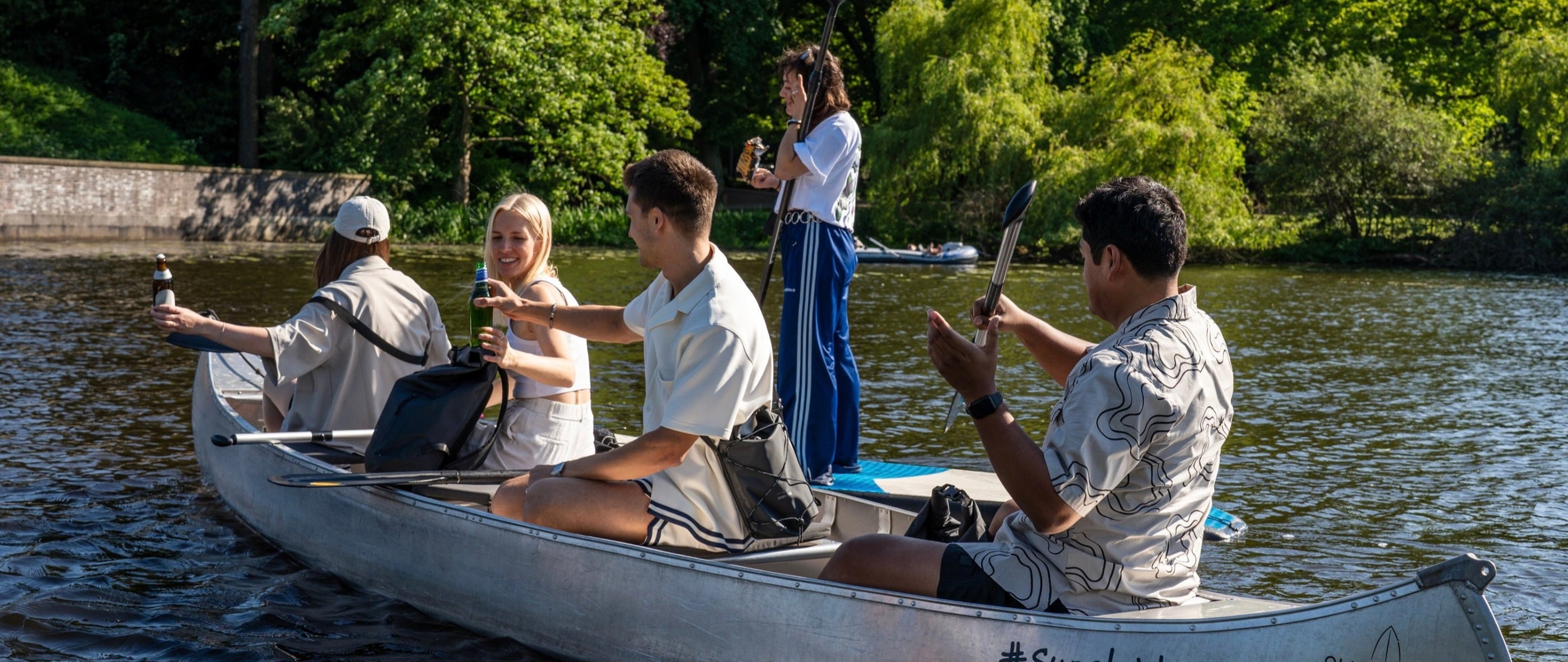 5 Freunde sind mit Kanu und Stand-Up-Paddle-Board auf der Hamburger Alster unterwegs und genießen das Wetter.
