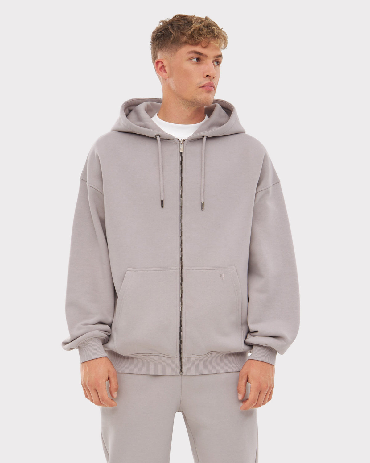 Mann trägt oversized Zip Hoodie 'Caleb' in Grau mit Kapuze, Reißverschluss und Kängurutaschen.