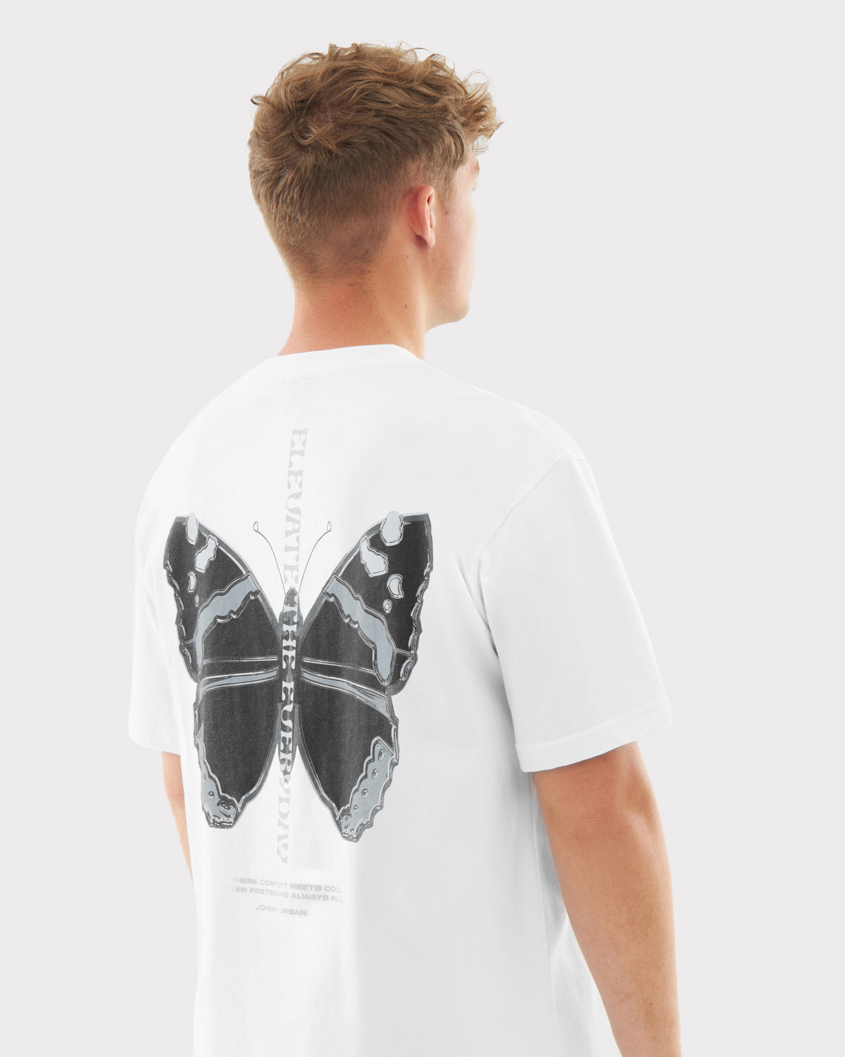 Junger Mann von hinten mit weißem Oversize-T-Shirt 'Sammy Chrome Butterfly' mit großem schwarzem Schmetterlingsdruck auf dem Rücken