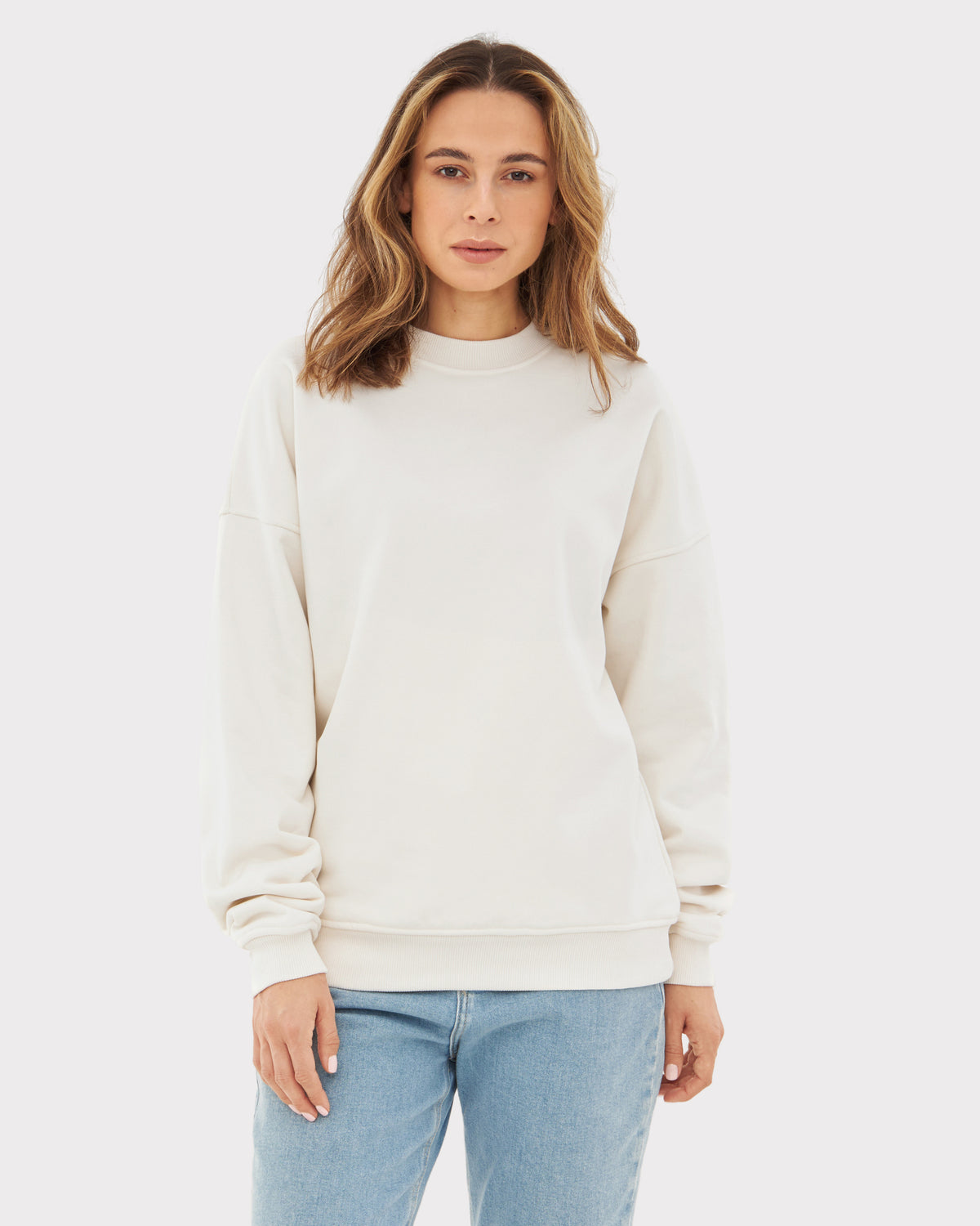Frau trägt oversized weißen Crewneck 'Carter' Sweatshirt mit langen Ärmeln und blauen Jeans