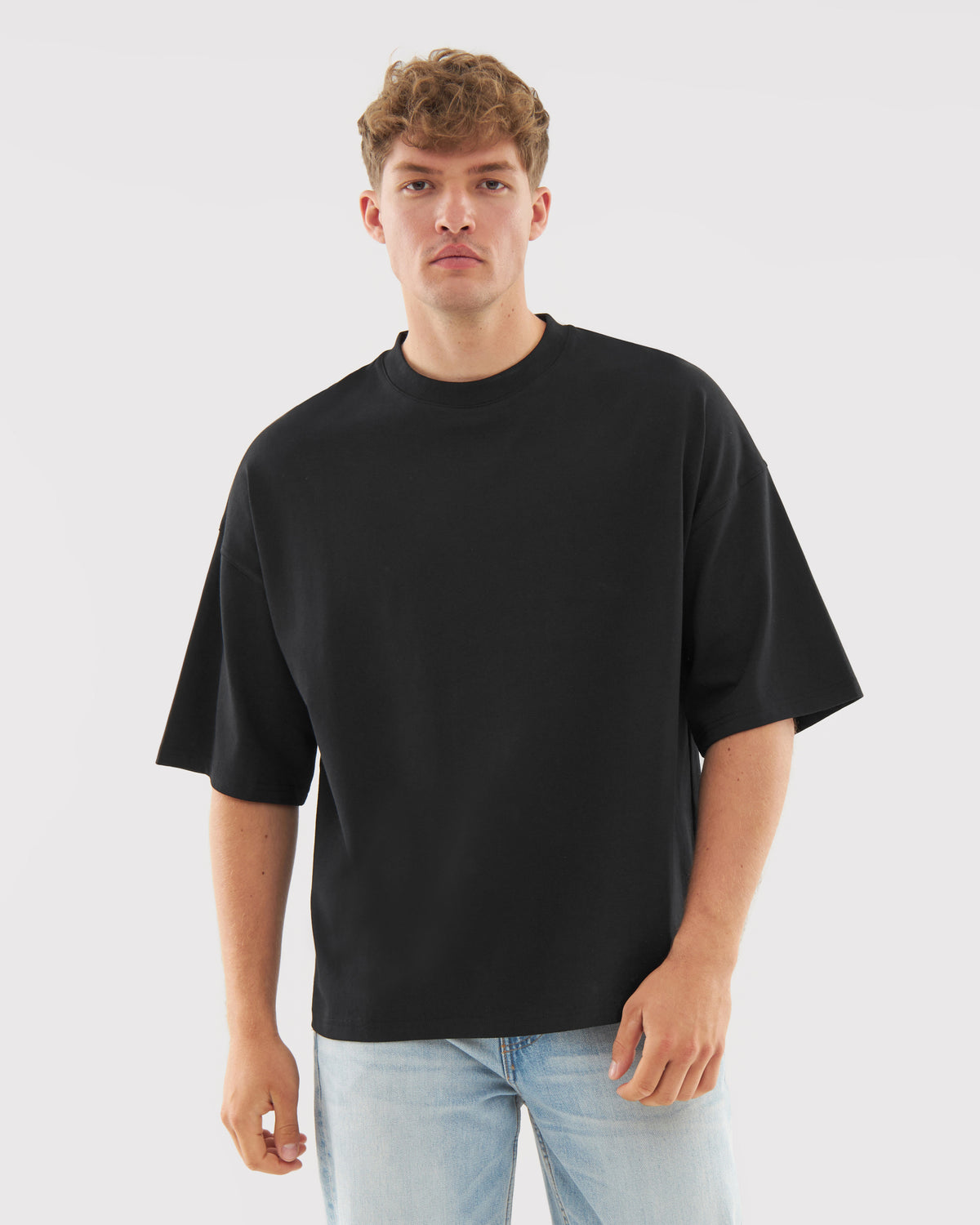 Mann trägt schwarzes T-Shirt 'Vic' mit lockerer Passform und kurzen Ärmeln, kombiniert mit hellblauen Jeans
