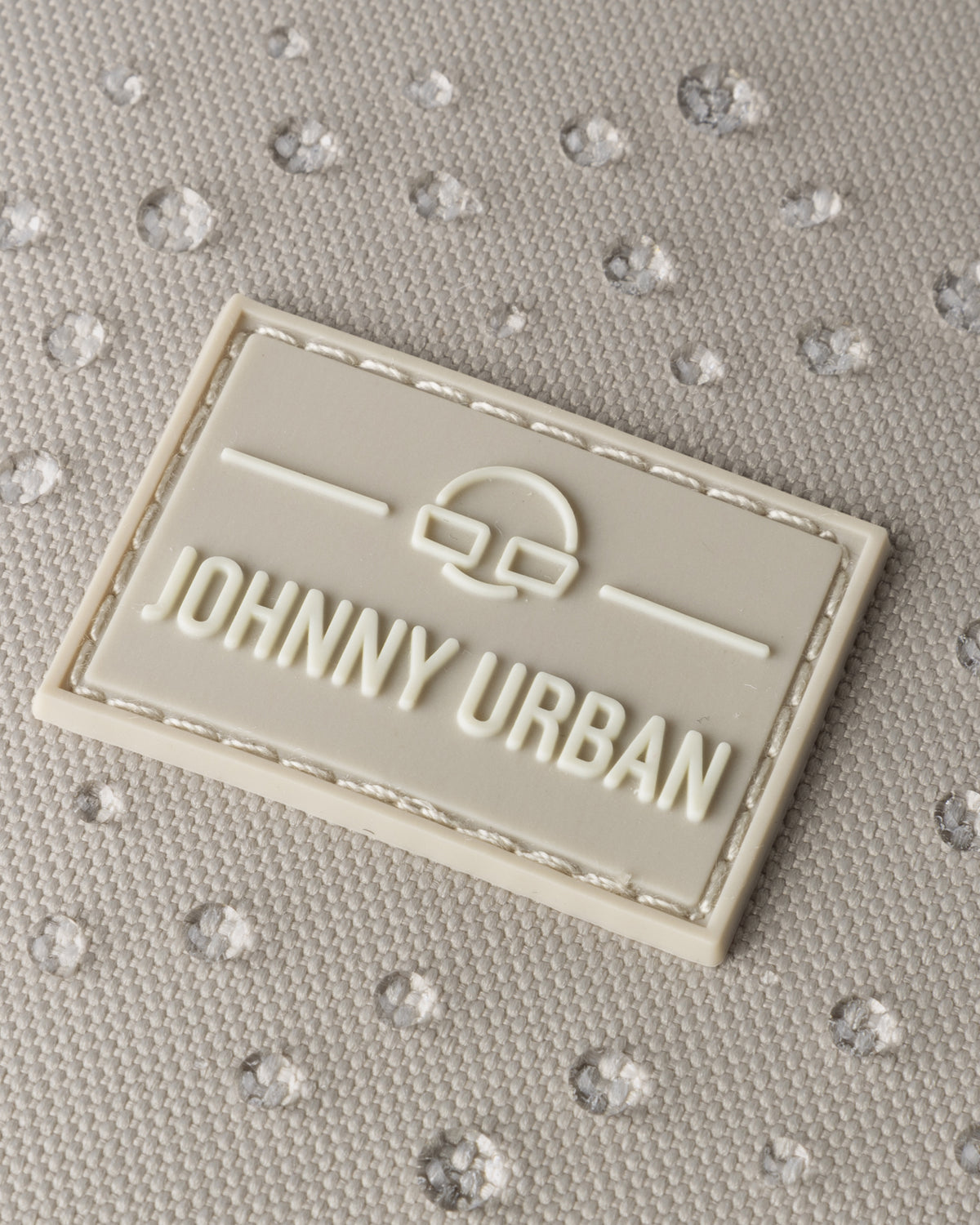 Nahaufnahme des Johnny Urban Logos auf Stoff mit Wasserperlen, zeigt wasserfesten Rucksack 'Nico'