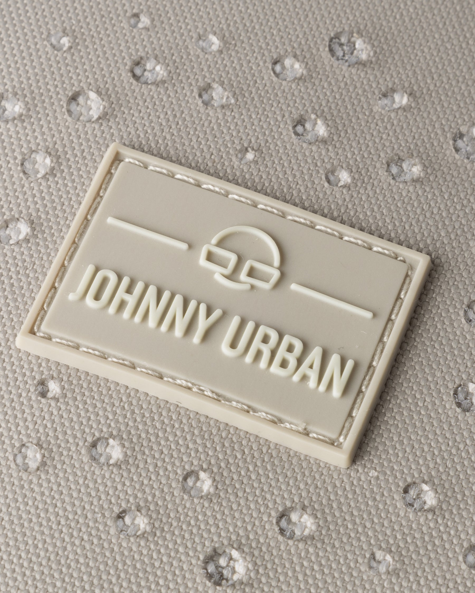 Nahaufnahme des Johnny Urban Logos auf Stoff mit Wasserperlen, zeigt wasserfesten Rucksack 'Nico'