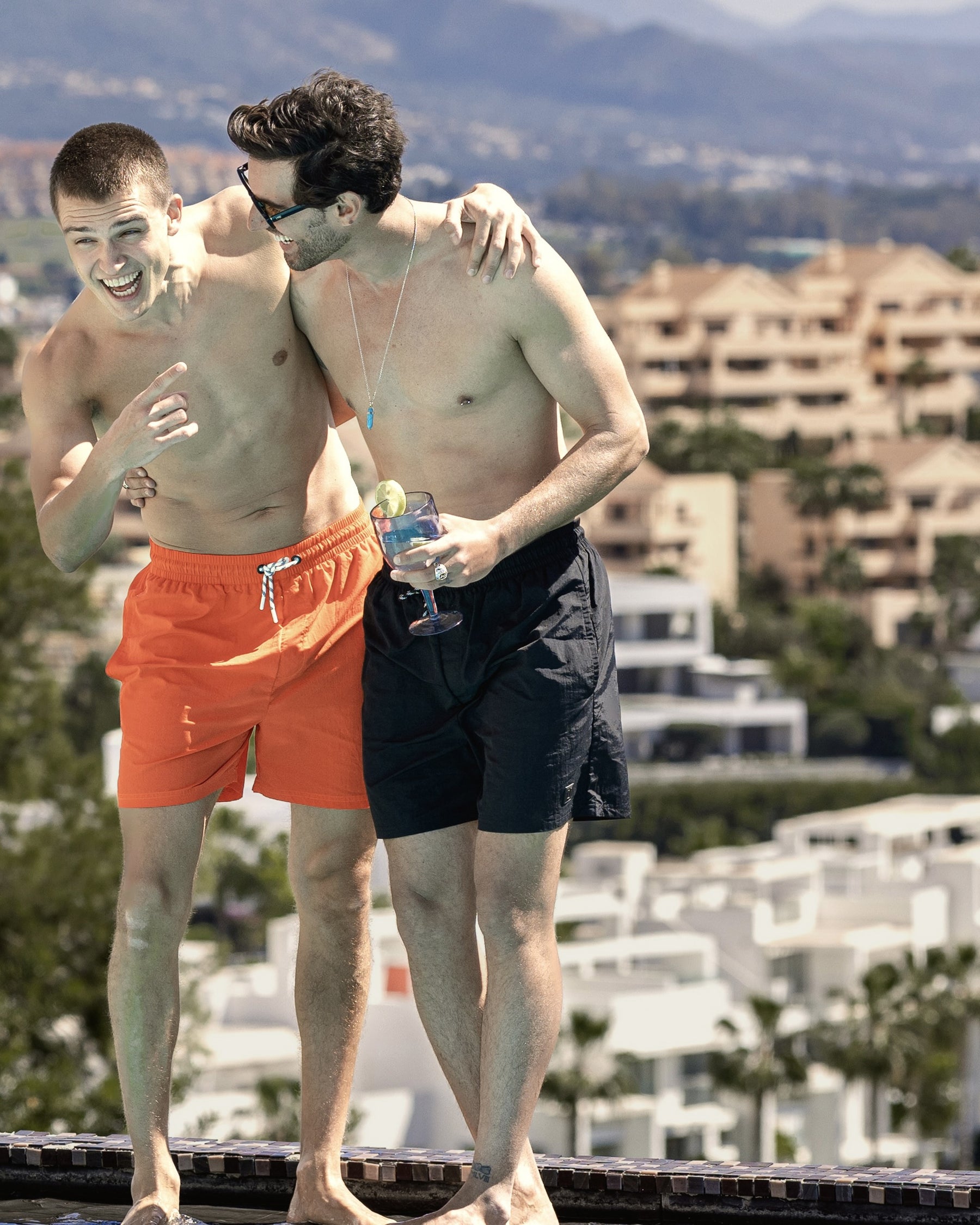 Zwei junge Männer am Pool, einer trägt die schwarze Badehose 'Jay', der andere eine orangefarbene Badehose.