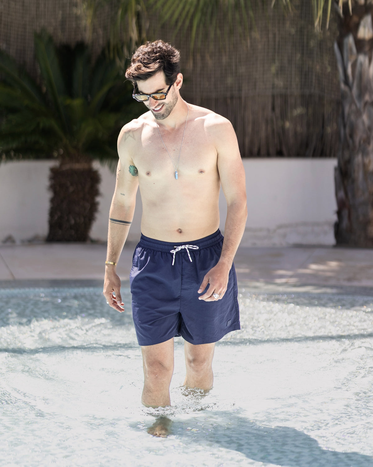 Mann trägt navyblaue Badehose 'Jay' und geht knietief im Poolwasser