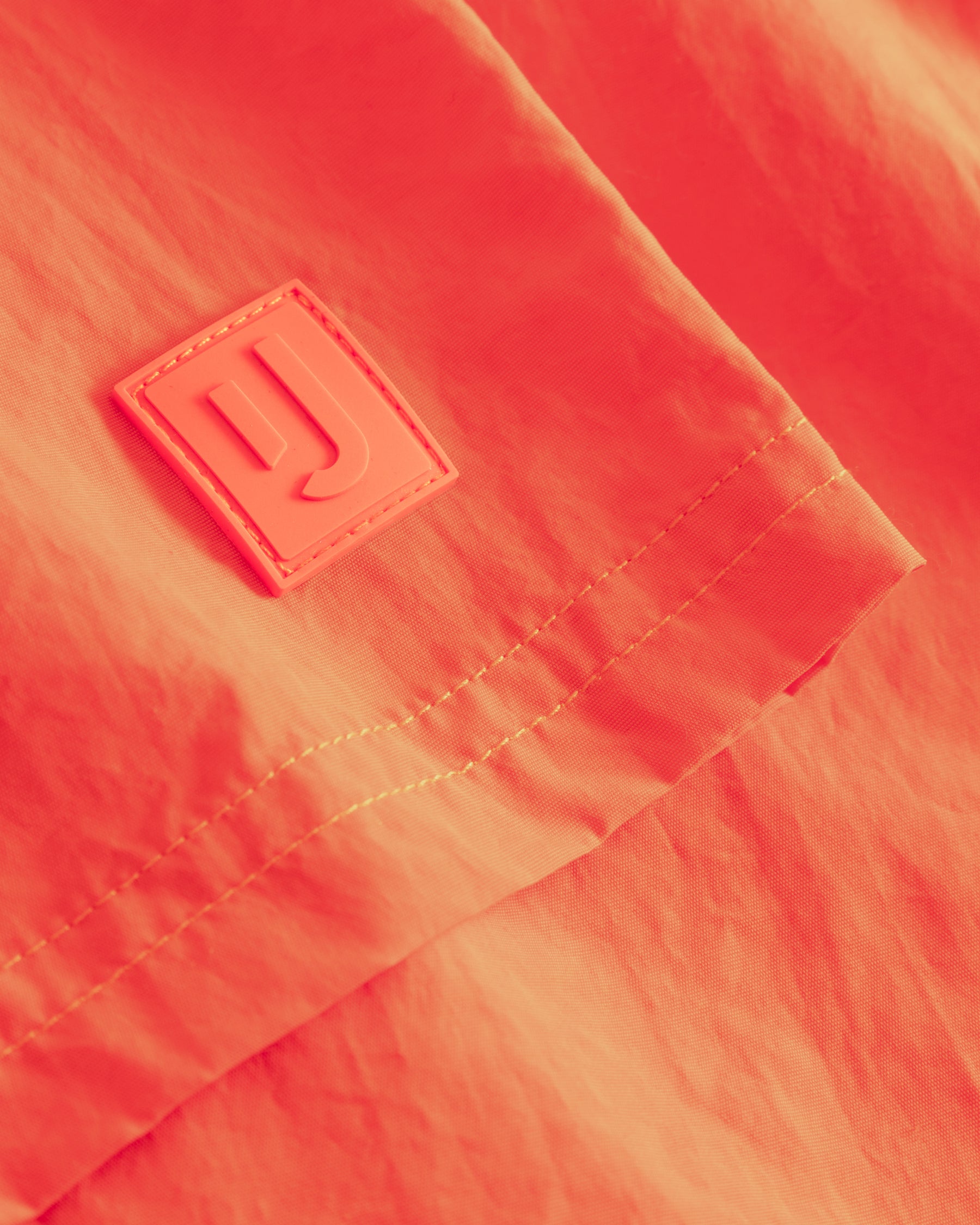 Nahaufnahme der orangen Badehose 'Jay' mit Johnny Urban Logo auf einem kleinen Aufnäher
