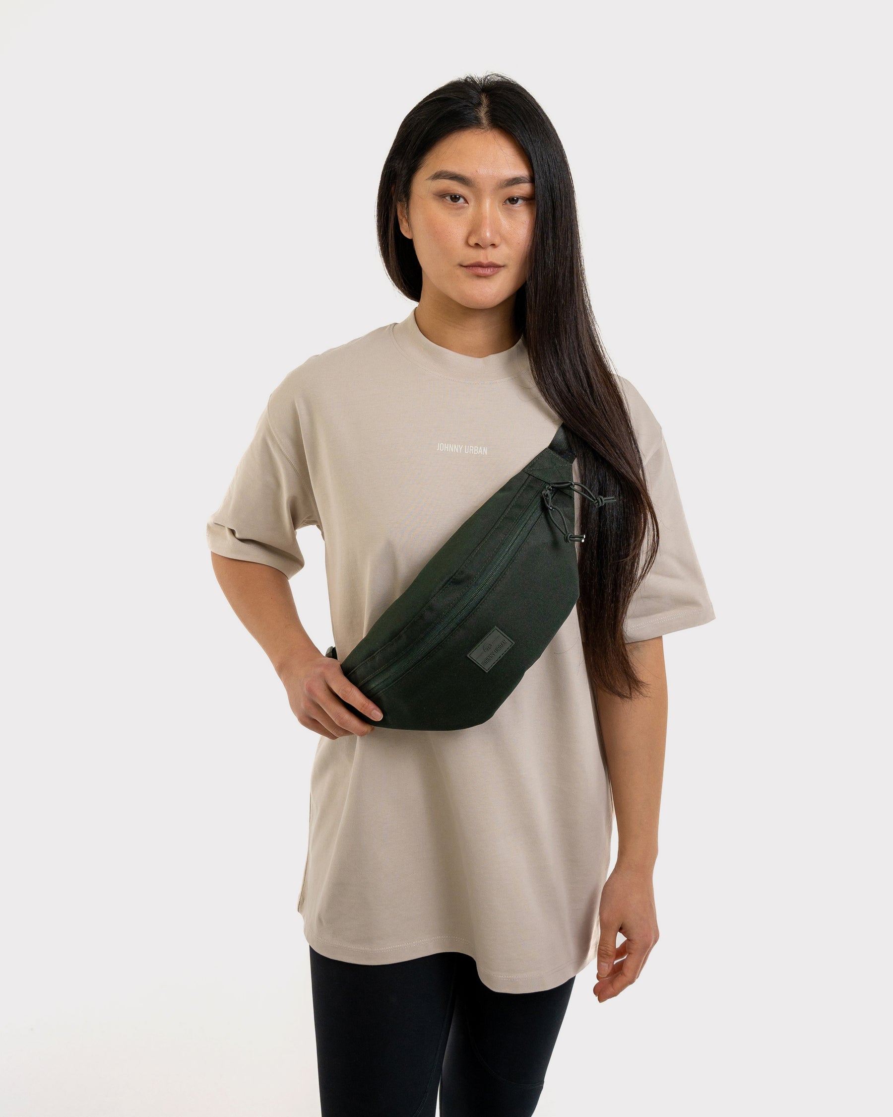 Frau trägt dunkelgrüne Johnny Urban Bauchtasche 'Erik Large' quer über die Brust, beige T-Shirt mit Logo