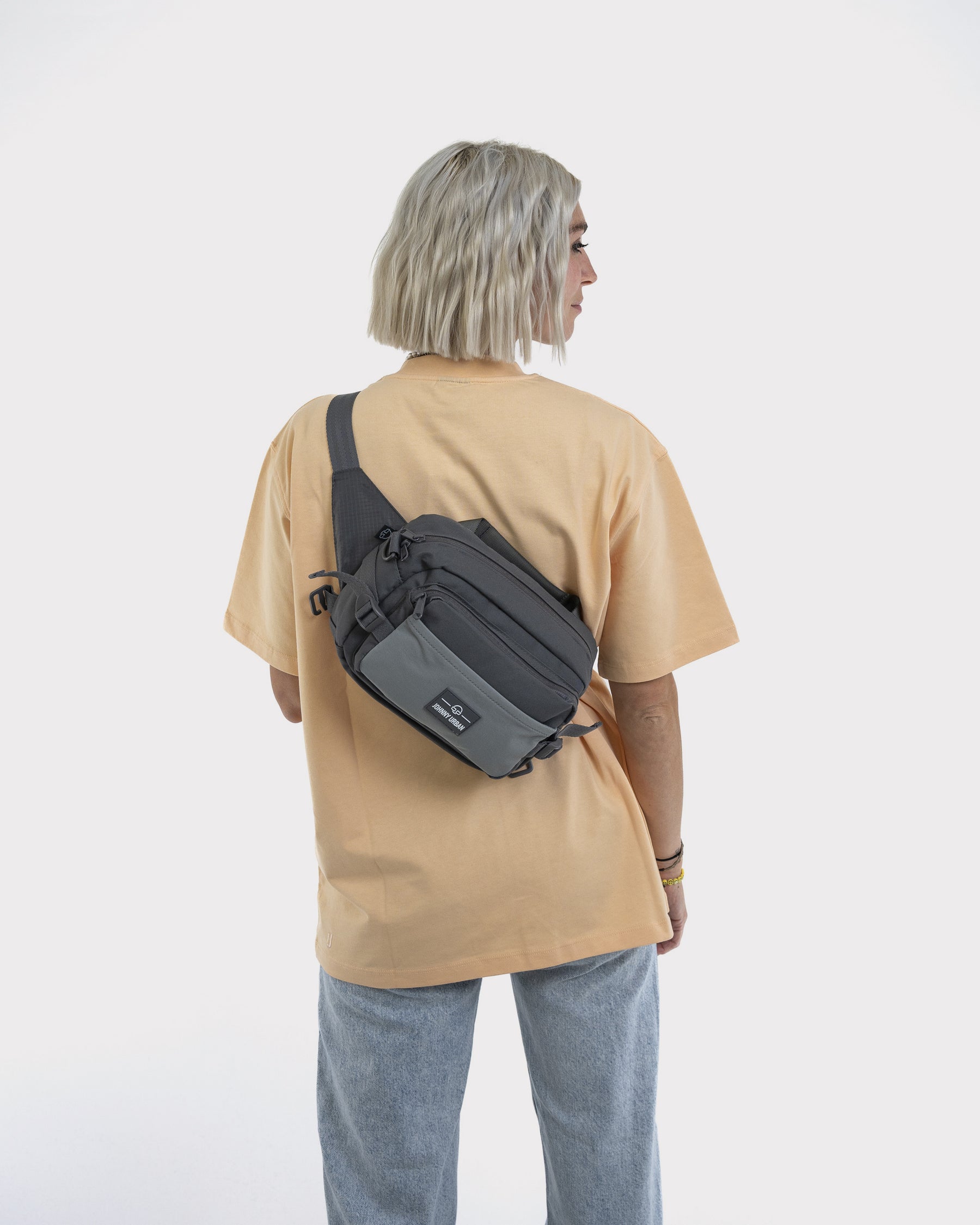 Frau mit hellblonden, kurzen gewellten Haaren trägt graue Bauchtasche 'Travis' von Johnny Urban quer über den Rücken