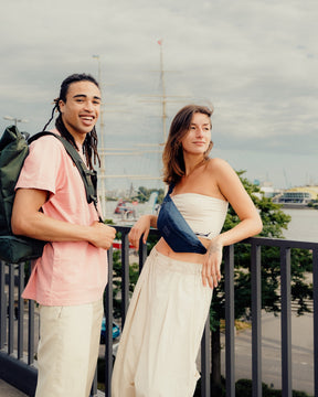 Junge Frau trägt die blaue Bauchtasche 'Erik Small' von Johnny Urban über dem Oberkörper, neben ihr steht ein junger Mann mit grünem Rucksack in urbaner Umgebung