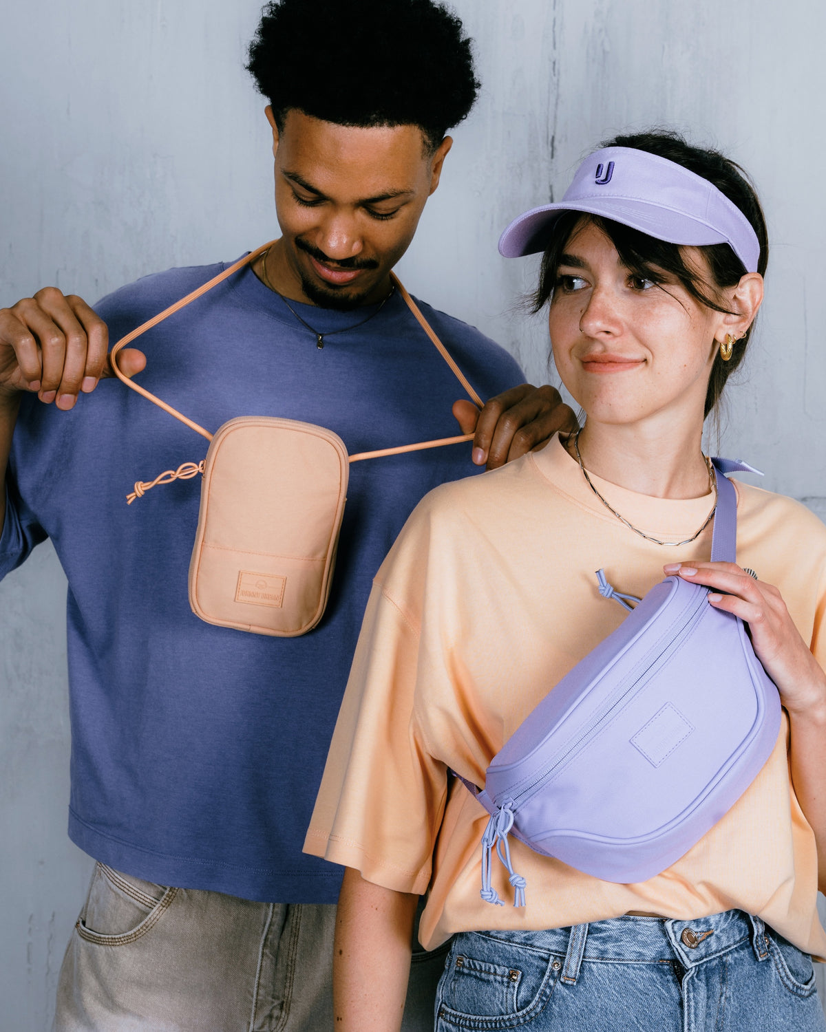 Mann trägt beige Bauchtasche Ben, Frau trägt lilafarbene Bauchtasche Ben und lila Visor