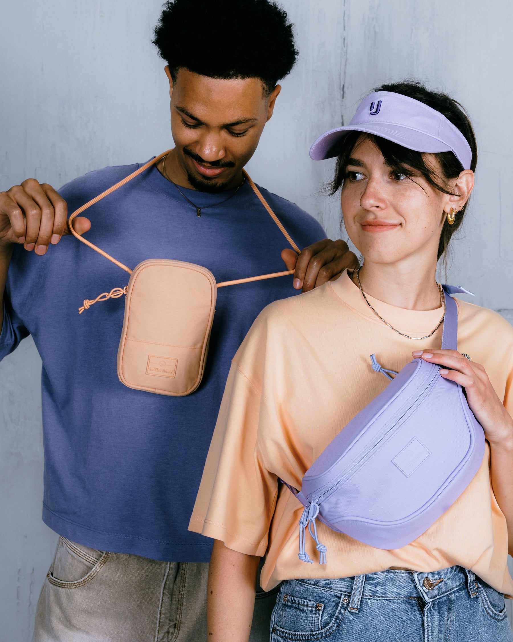 Mann trägt beige Bauchtasche Ben, Frau trägt lilafarbene Bauchtasche Ben und lila Visor