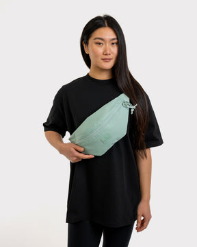 Frau trägt mintgrüne Bauchtasche ‚Erik Large‘ von Johnny Urban über der schwarzen Oversize-Tunika