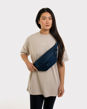 Frau trägt blaue Johnny Urban Bauchtasche 'Erik Large' quer über dem beigen T-Shirt