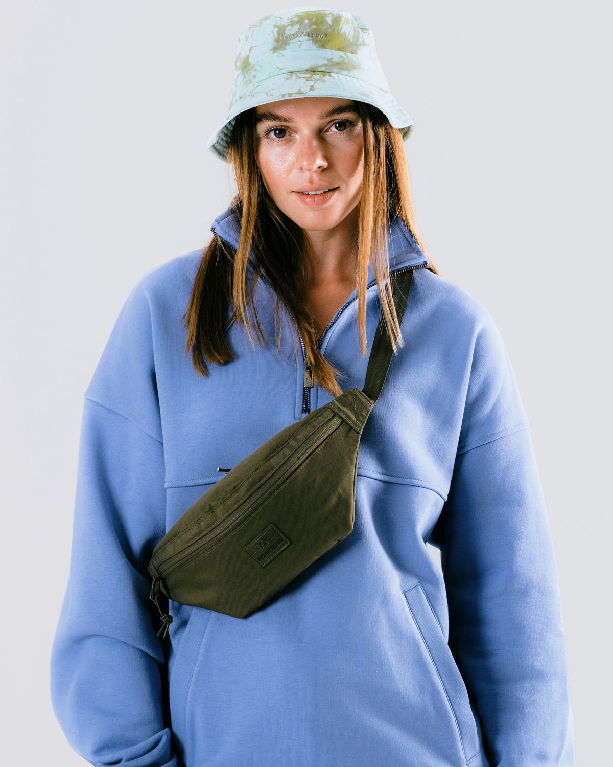 Frau trägt olivgrüne Johnny Urban Bauchtasche 'Erik Small' über blauem Pullover mit Reißverschluss