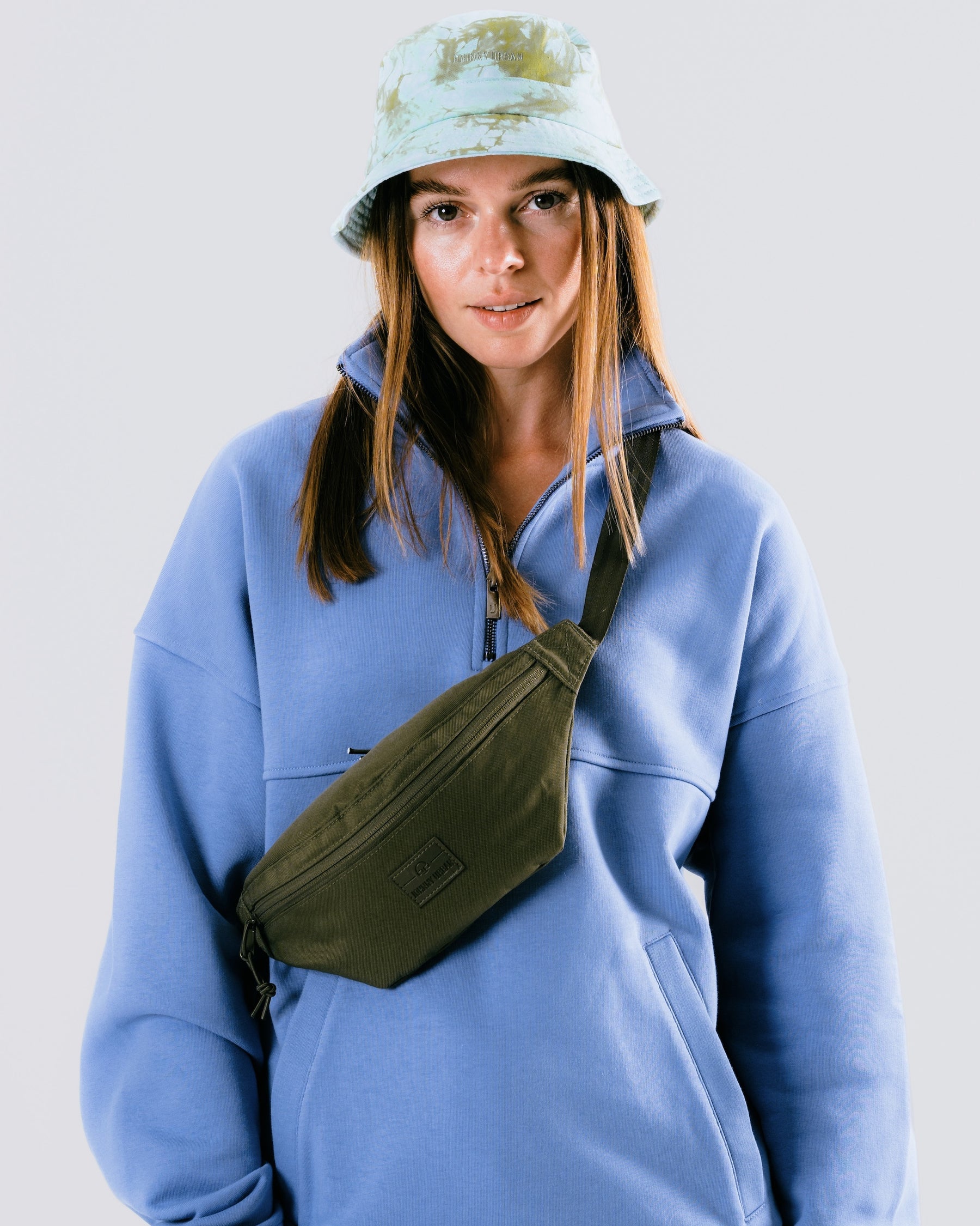 Frau trägt olivgrüne Johnny Urban Bauchtasche 'Erik Small' über blauem Pullover mit Reißverschluss