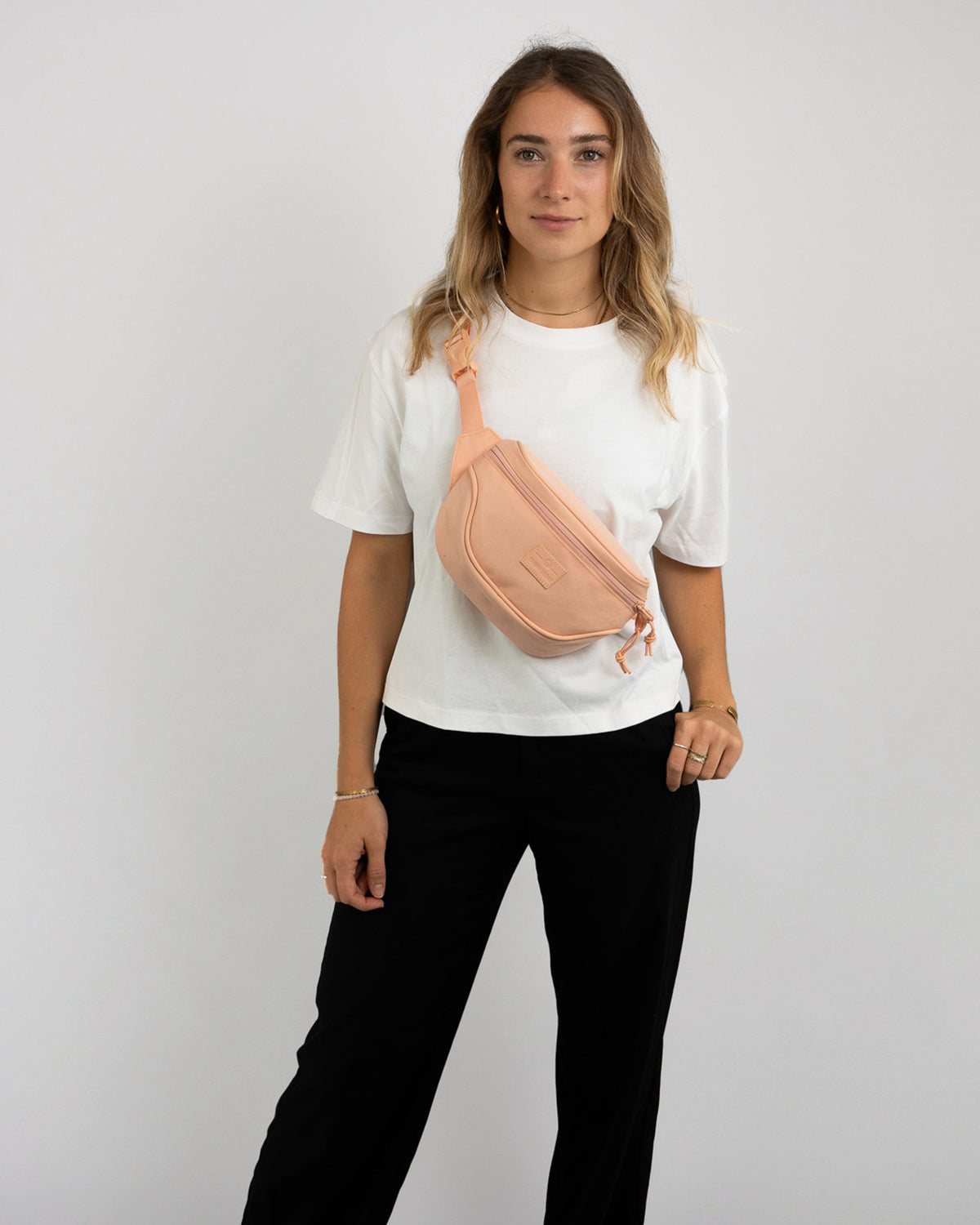 Frau trägt peachfarbene Bauchtasche 'Ben' von Johnny Urban über weiße T-Shirt und schwarze Hose