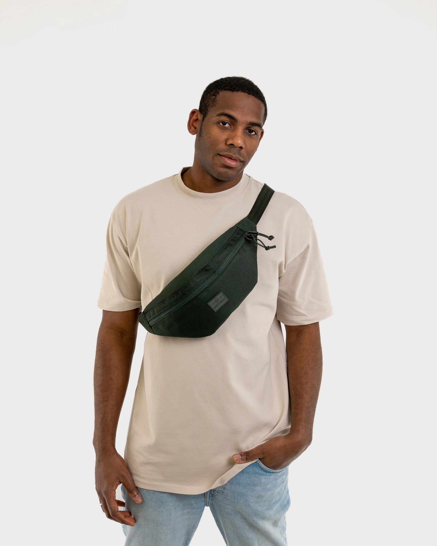 Mann trägt dunkelgrüne Johnny Urban Bauchtasche 'Erik Large' quer über die Brust mit beige T-Shirt und Jeans