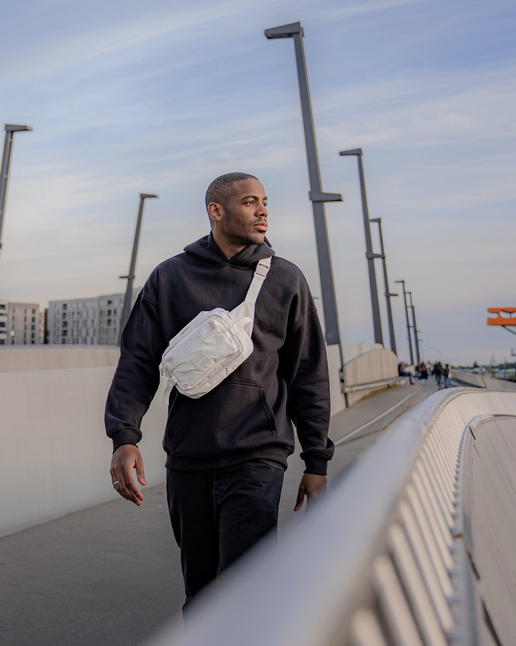 Mann trägt beigen Bauchtasche 'Travis' von Johnny Urban über schwarzem Hoodie auf urbaner Brücke
