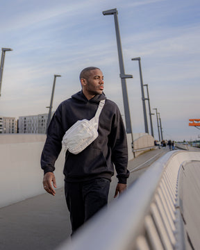 Mann trägt beigen Bauchtasche 'Travis' von Johnny Urban über schwarzem Hoodie auf urbaner Brücke