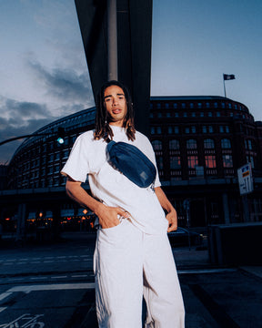 Mann mit blauer Johnny Urban Bauchtasche 'Tom' über weißem T-Shirt in urbaner Abendumgebung