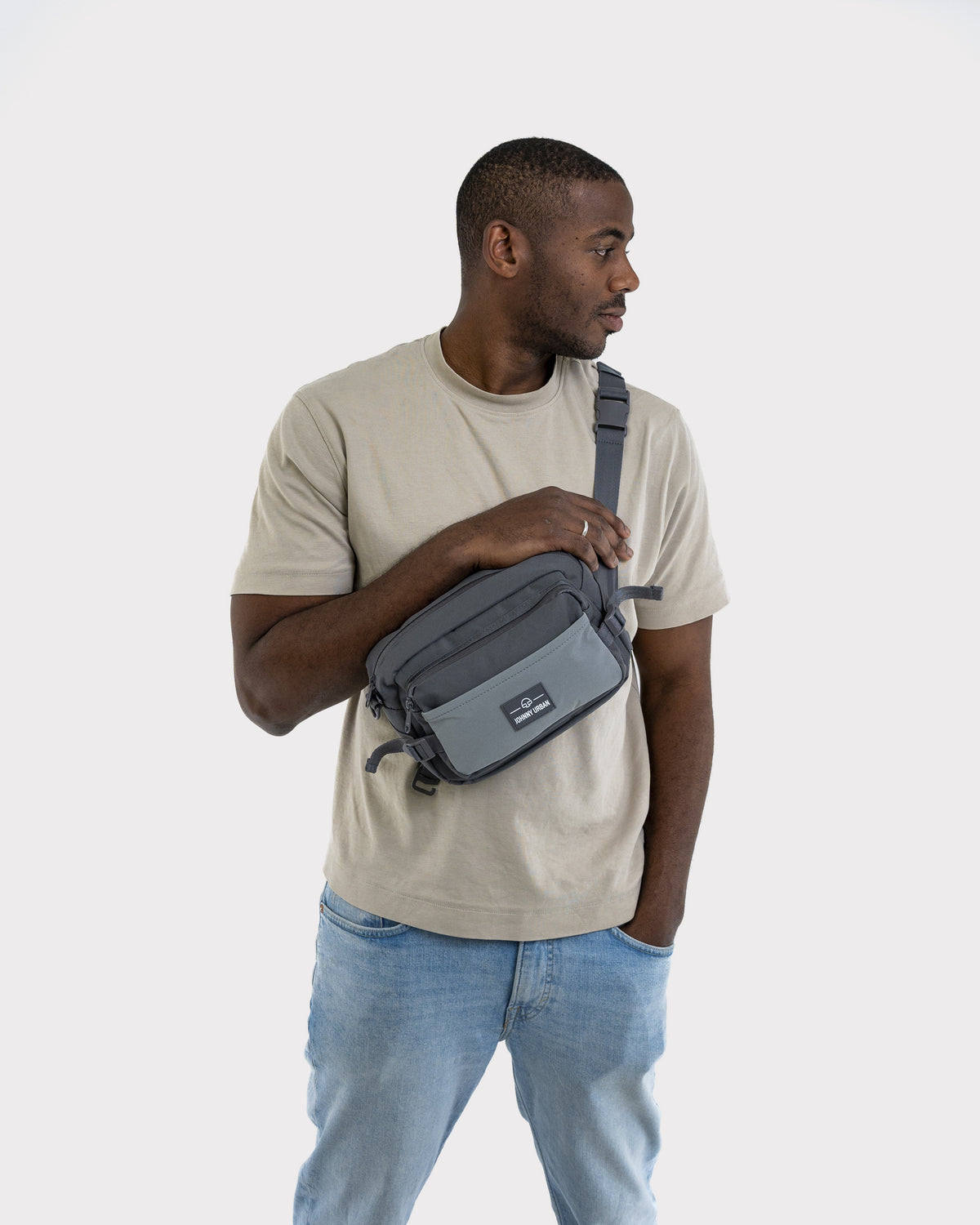 Mann trägt graue Johnny Urban Bauchtasche 'Travis' quer vor der Brust mit hellbeigem T-Shirt und Jeans