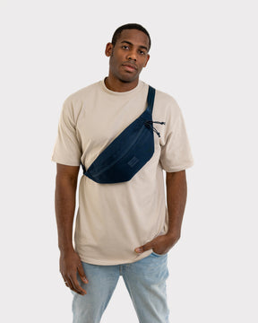 Mann trägt moderne blaue Bauchtasche 'Erik Large' von Johnny Urban quer über der Brust, beige T-Shirt, helle Jeans