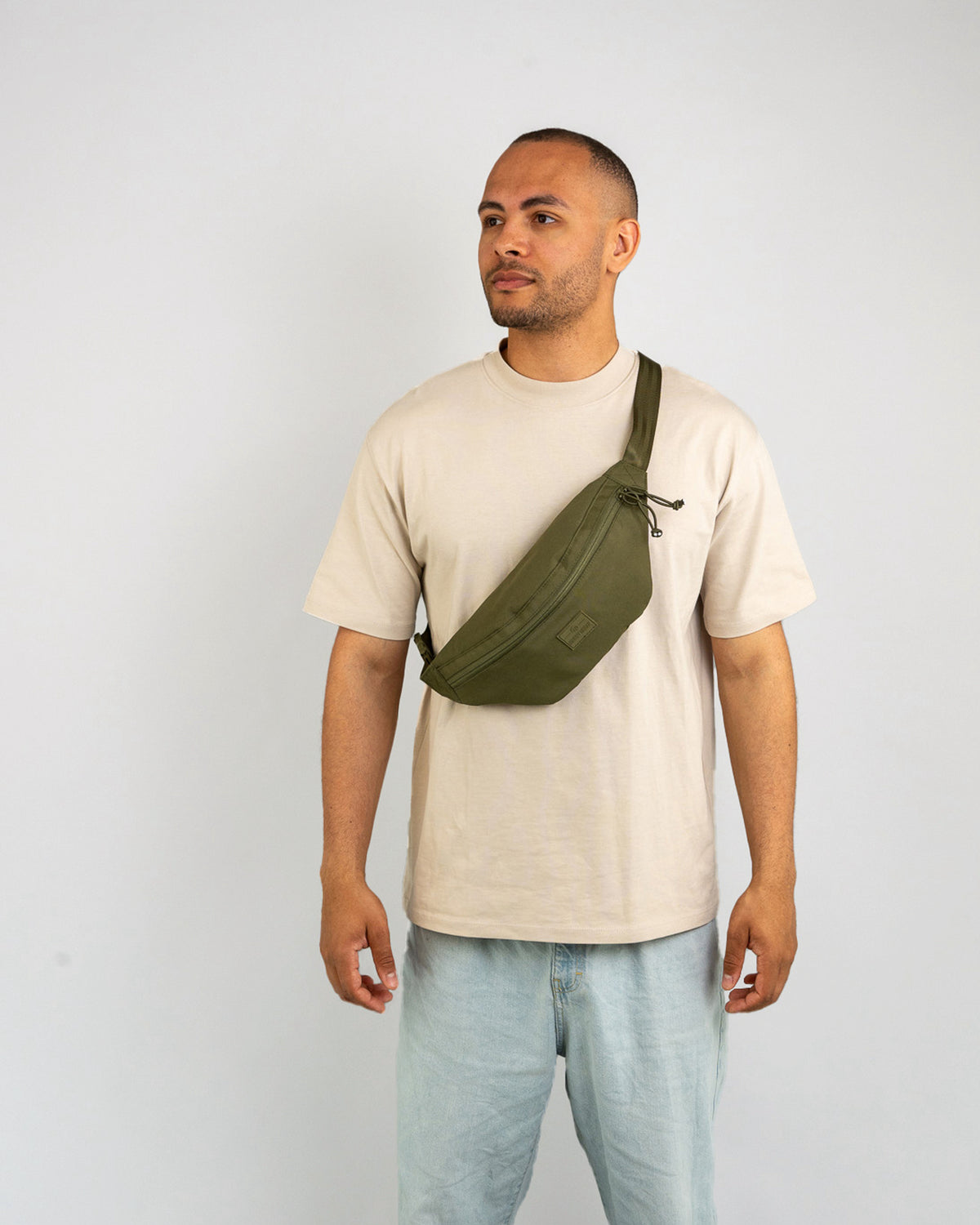 Mann trägt olivgrüne Bauchtasche ‚Erik Large‘ quer über der Brust mit hellem T-Shirt und Jeans