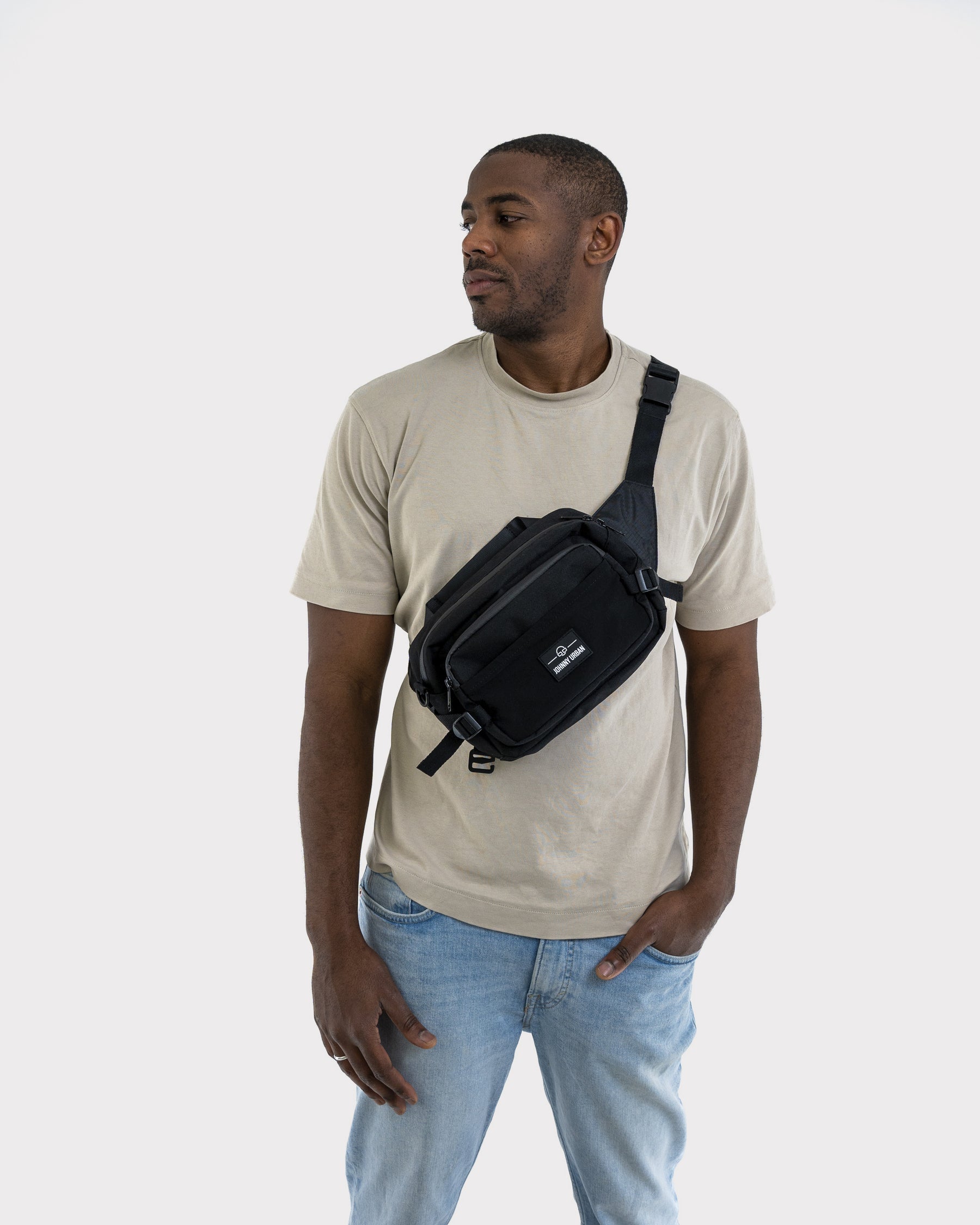 Mann trägt schwarze Johnny Urban Bauchtasche 'Travis' quer über die Brust über beigem T-Shirt und blauer Jeans