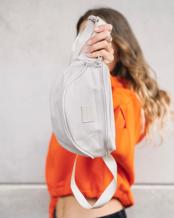 Frau in orangem Pulli hält eine Johnny Urban Bauchtasche in die Kamera. 
