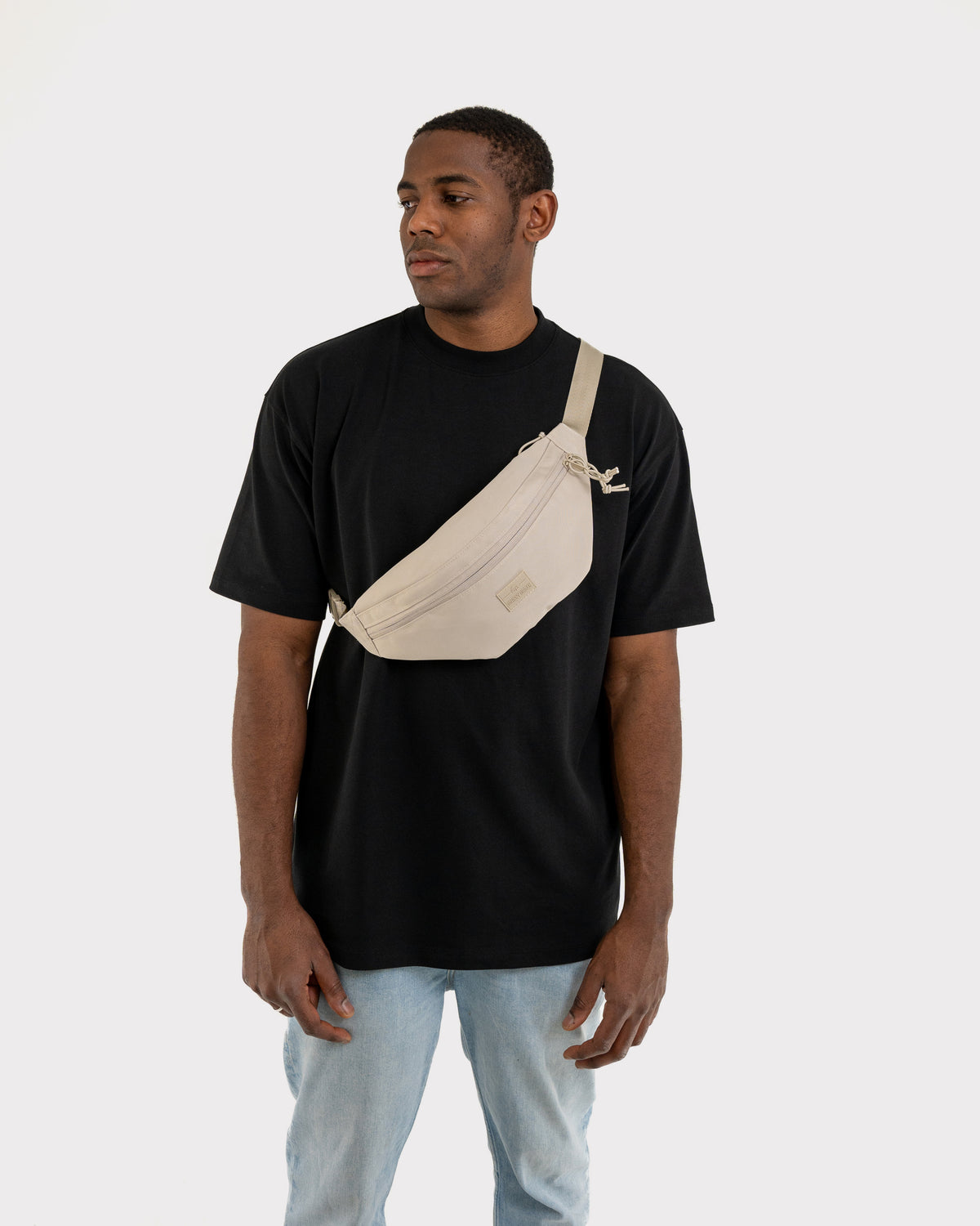 Mann trägt beige Bauchtasche 'Erik Large' von Johnny Urban quer über der Brust zu schwarzem T-Shirt und blauen Jeans