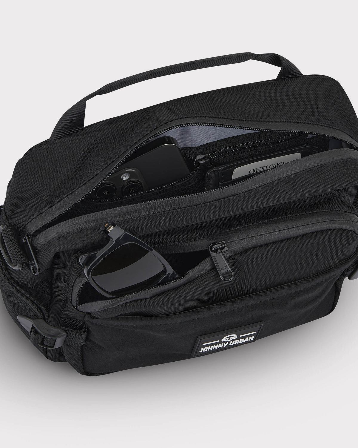 Schwarze Bauchtasche 'Travis' von Johnny Urban mit geöffneten Reißverschlusstaschen, darin Smartphone, Kreditkarte und Sonnenbrille