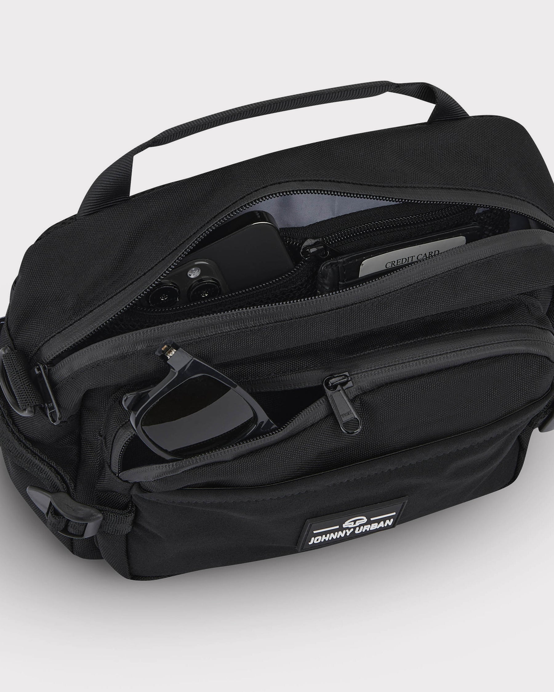 Schwarze Bauchtasche 'Travis' von Johnny Urban mit geöffneten Reißverschlusstaschen, darin Smartphone, Kreditkarte und Sonnenbrille