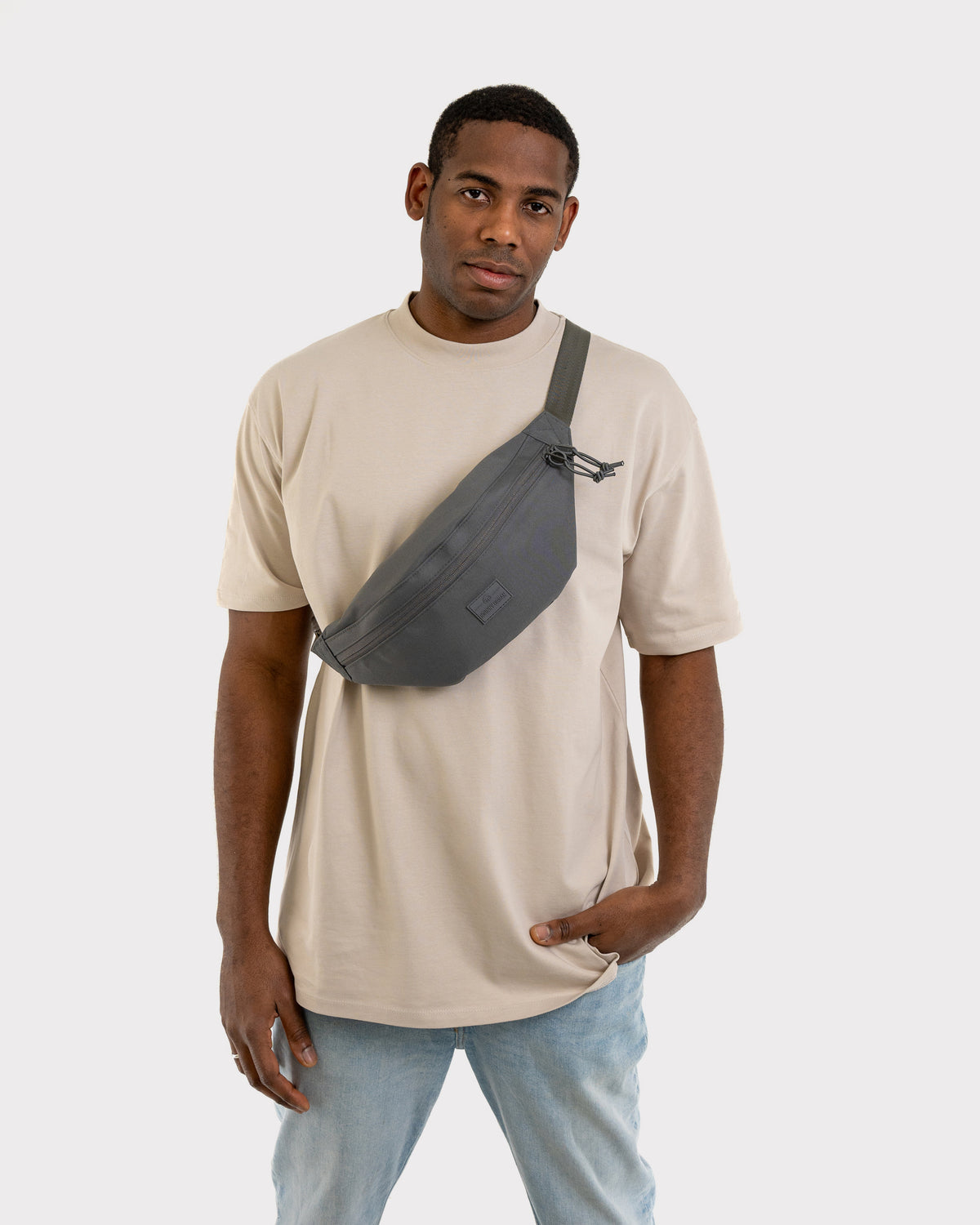 Mann trägt dunkelgraue Bauchtasche 'Erik Large' von Johnny Urban diagonal über beige T-Shirt und Jeans