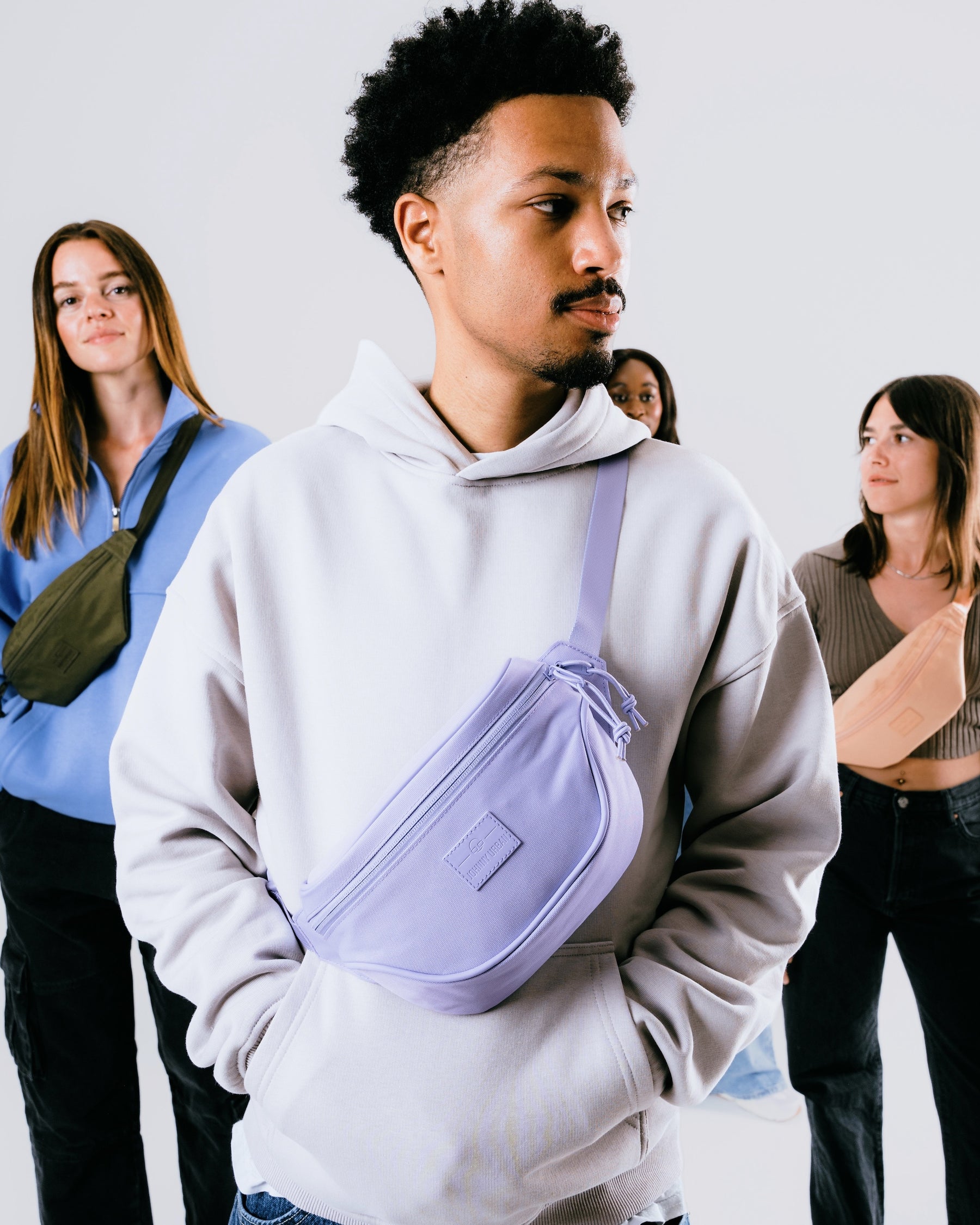 Vier Personen tragen die Bauchtasche 'Ben' in lila, olivgrün, pfirsich und schwarz, urbaner Stil