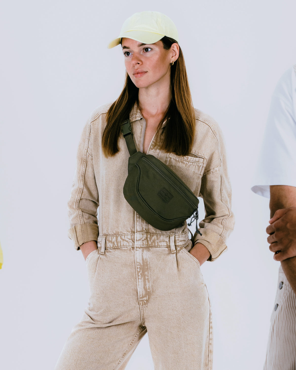 Frau mit hellbeigem Overall und olivgrüner Bauchtasche 'Ben', trägt beige Kappe