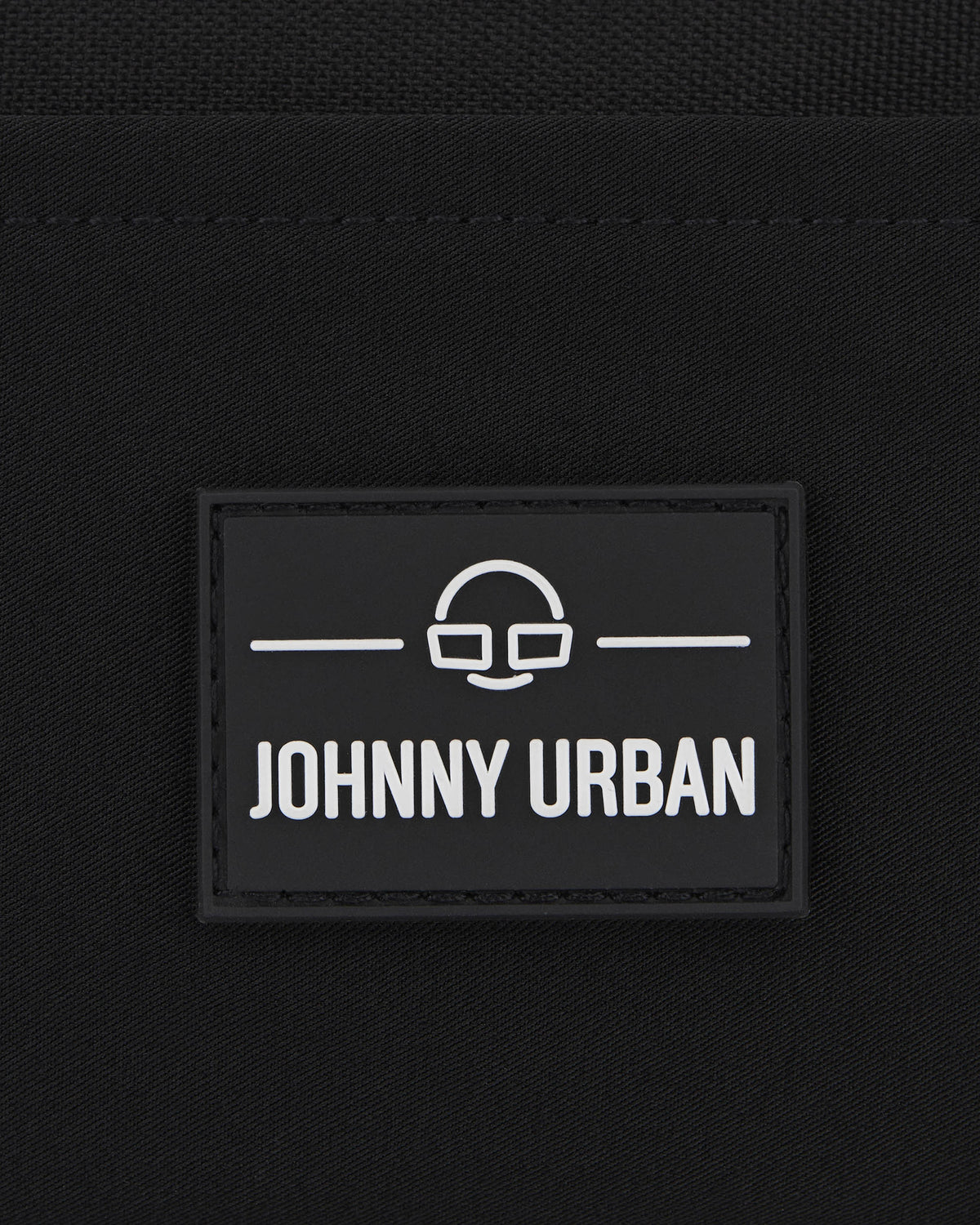 Schwarzes Logoetikett mit weißem Johnny Urban Schriftzug und minimalistischer Brillen-Motiv auf Stoff