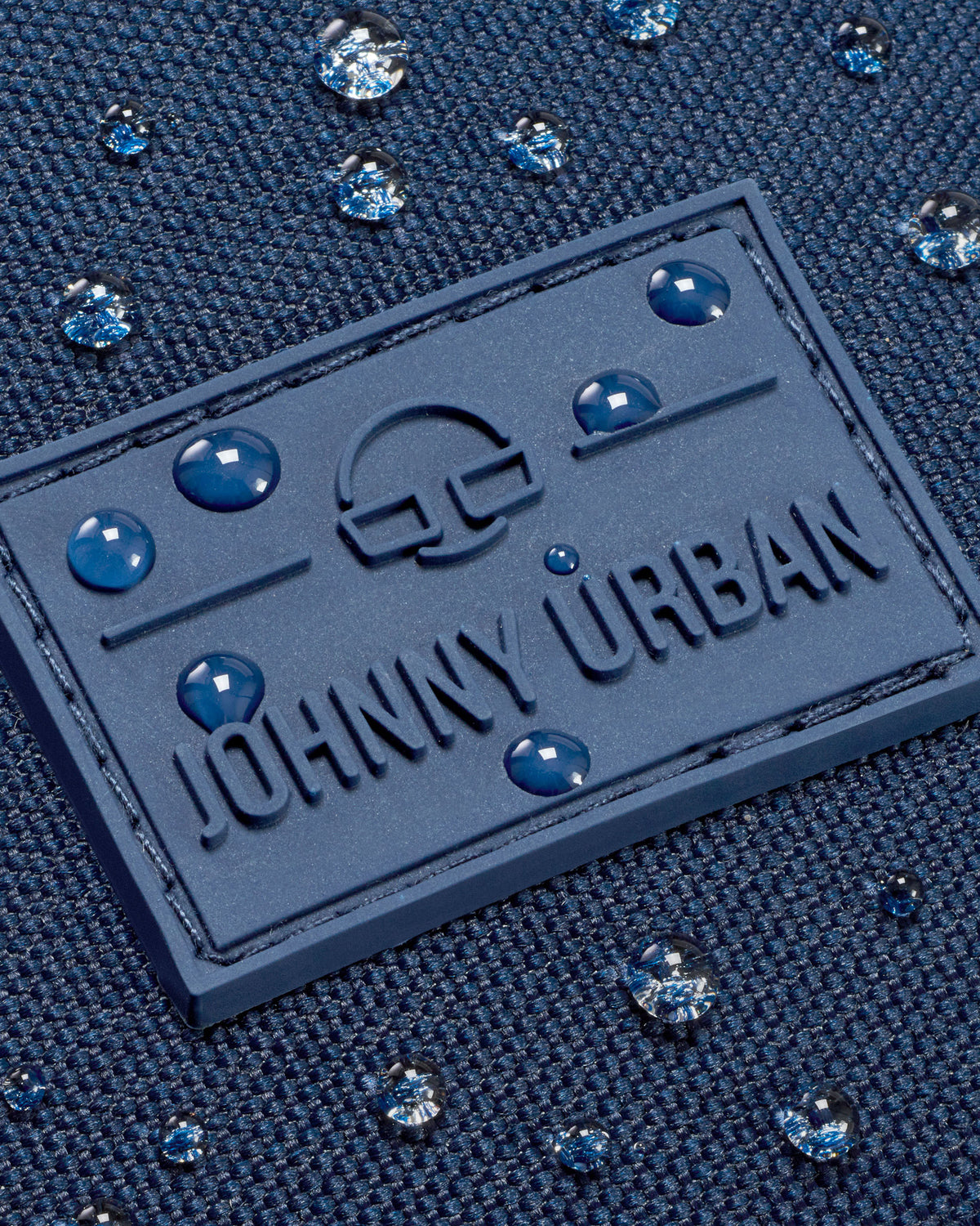 Nahaufnahme des wasserdichten blauen Gewebes mit Johnny Urban Logo und Wassertröpfchen auf der Bauchtasche Erik Large