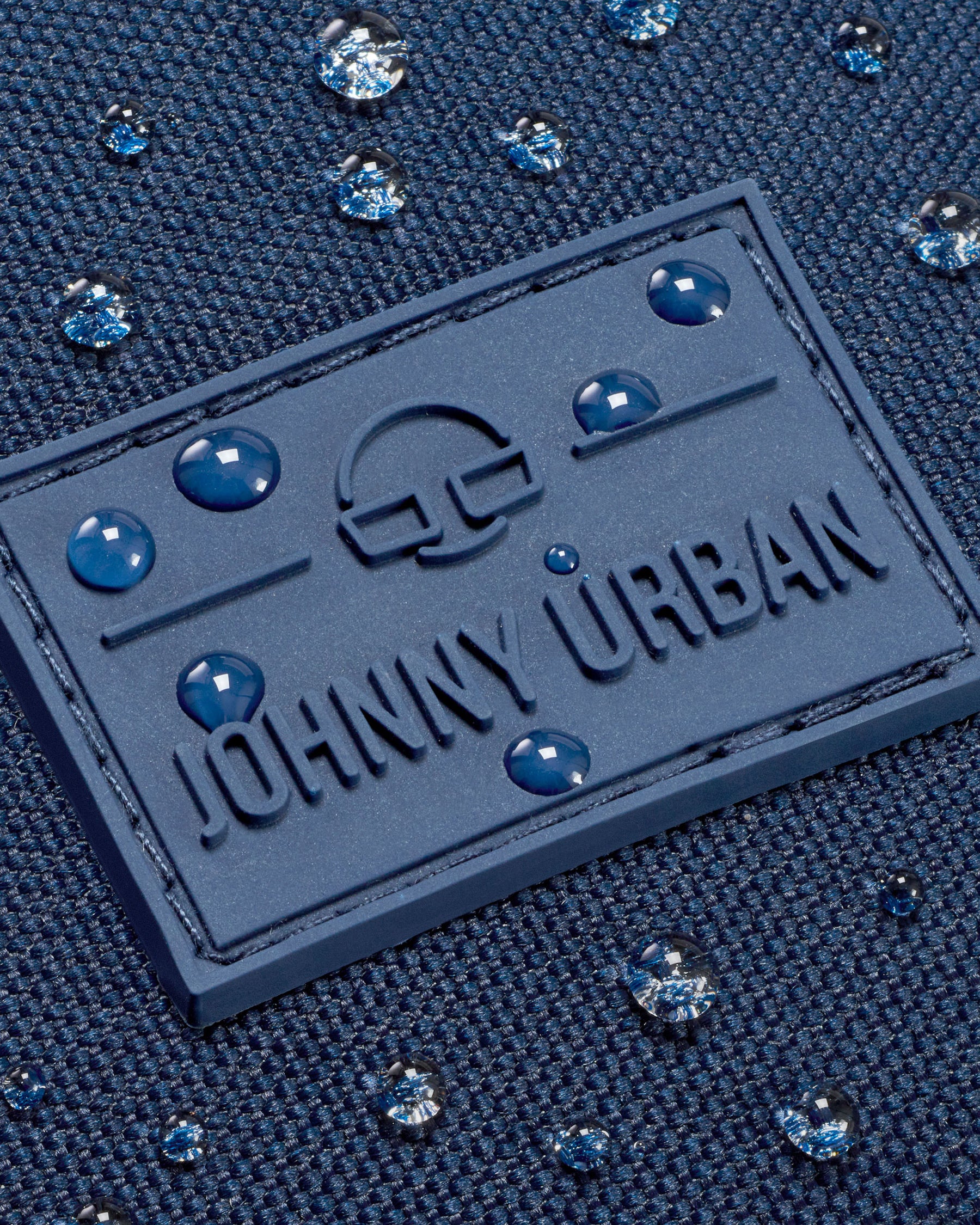 Nahaufnahme des wasserdichten blauen Gewebes mit Johnny Urban Logo und Wassertröpfchen auf der Bauchtasche Erik Large