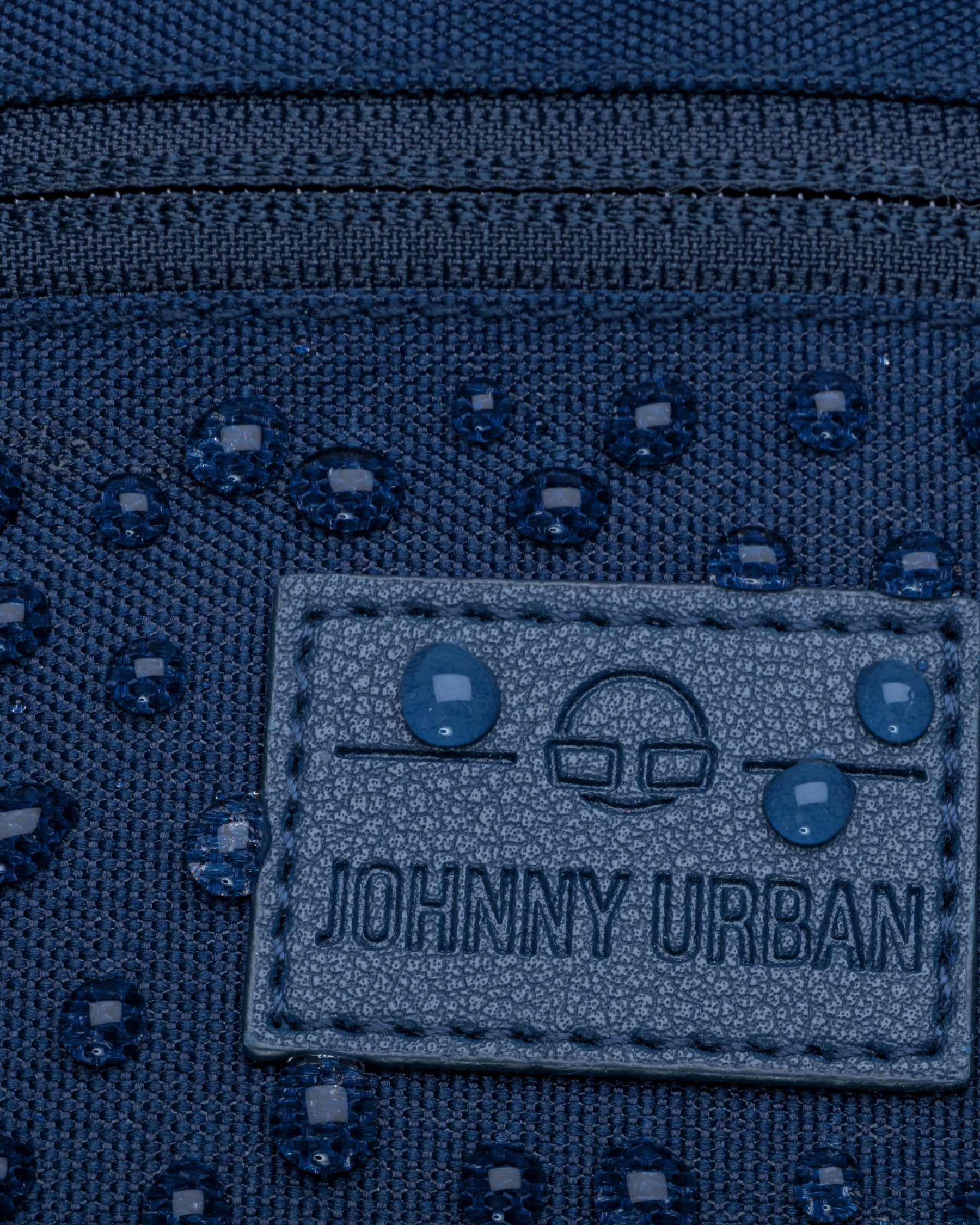 Detailaufnahme der wasserabweisenden blauen Bauchtasche „Erik Small“ von Johnny Urban mit sichtbaren Wassertropfen und Markenlabel