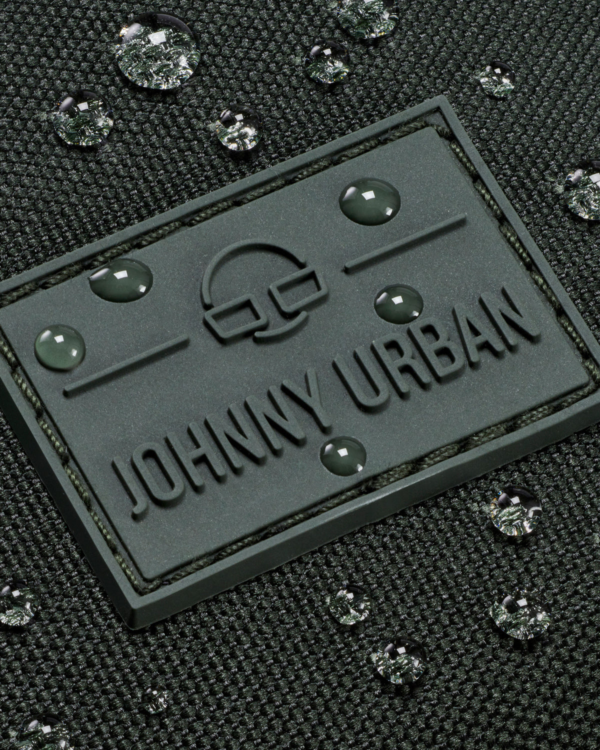 Gummilogo mit Schriftzug 'Johnny Urban' auf wasserabweisendem dunkelgrünem Stoff mit Wassertropfen