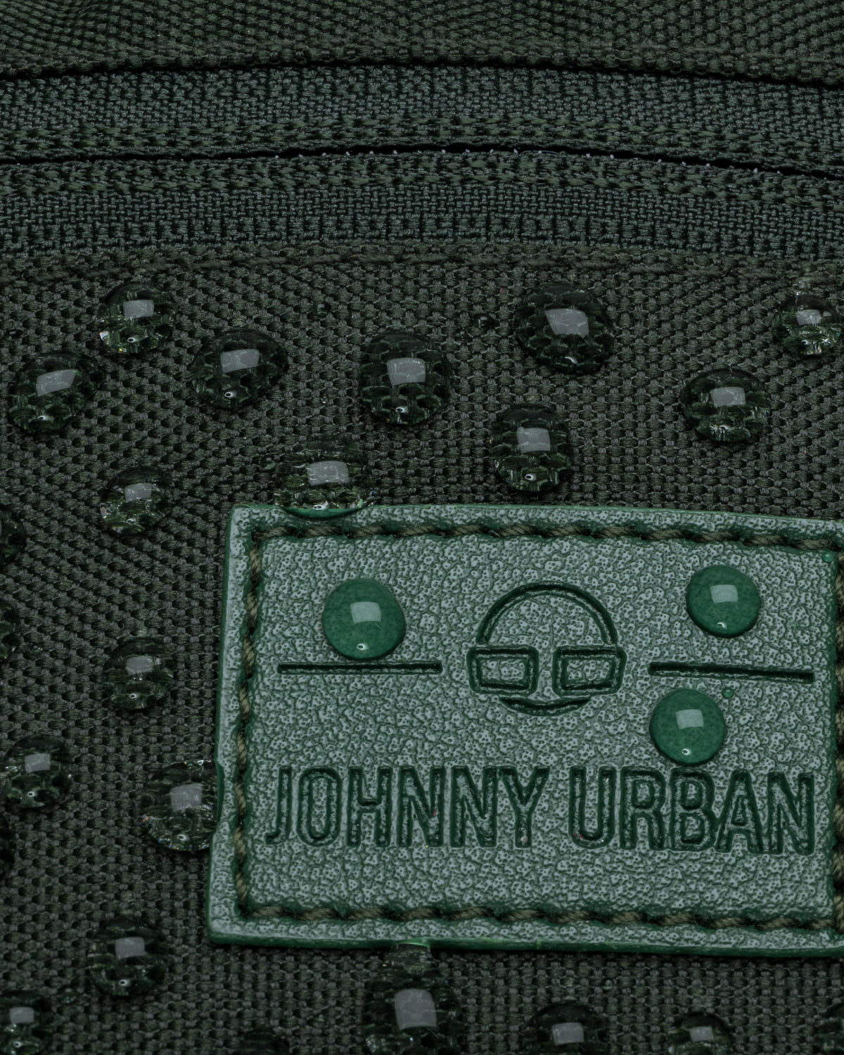 Nahaufnahme der wasserabweisenden grünen Johnny Urban Bauchtasche 'Erik Small' mit Wassertropfen auf dem Logo