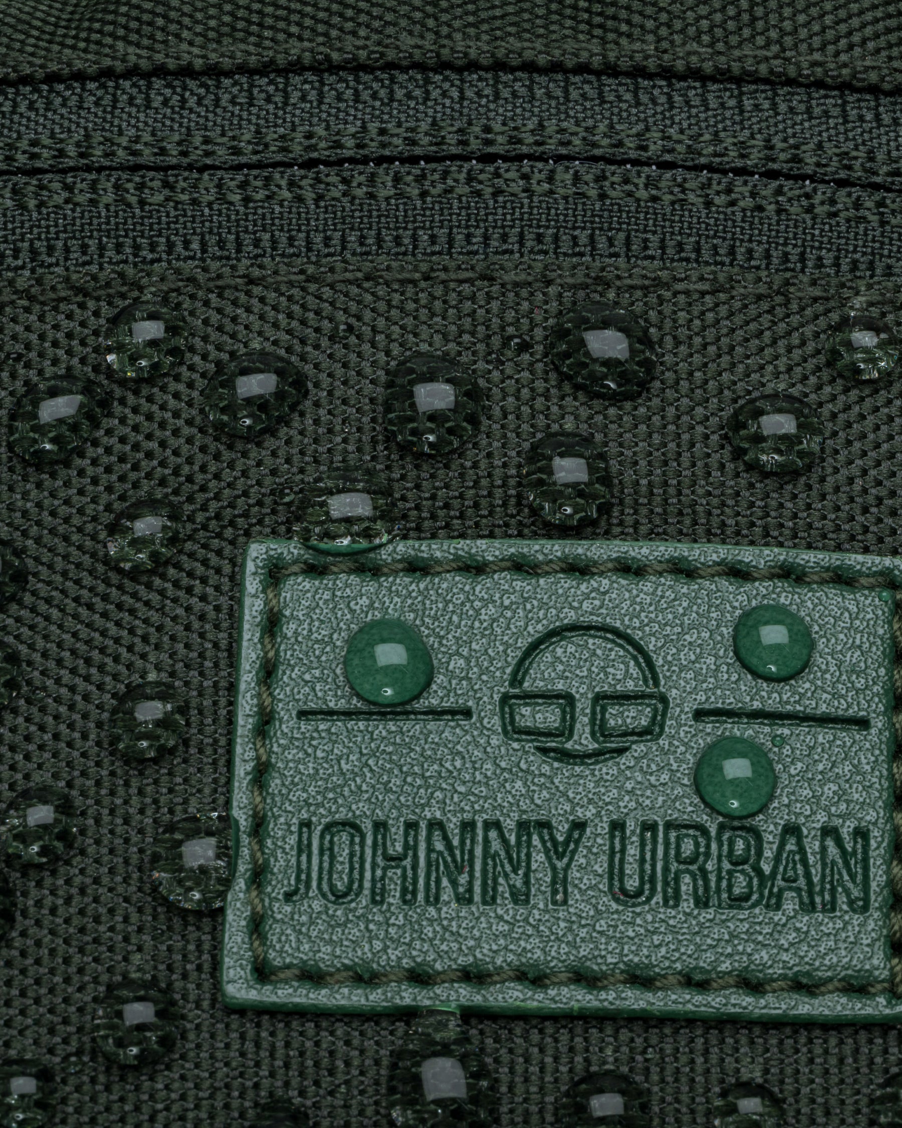 Nahaufnahme der wasserabweisenden grünen Johnny Urban Bauchtasche 'Erik Small' mit Wassertropfen auf dem Logo
