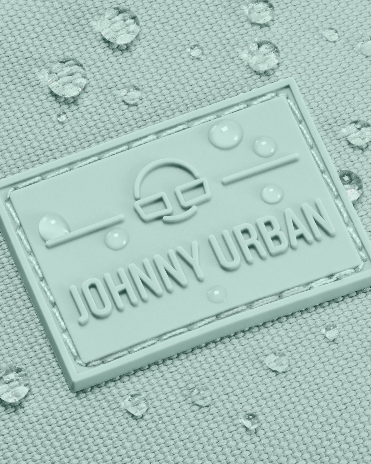 Nahaufnahme des wasserabweisenden Johnny Urban Logos auf der mintfarbenen Bauchtasche 'Erik Large' mit Wassertropfen