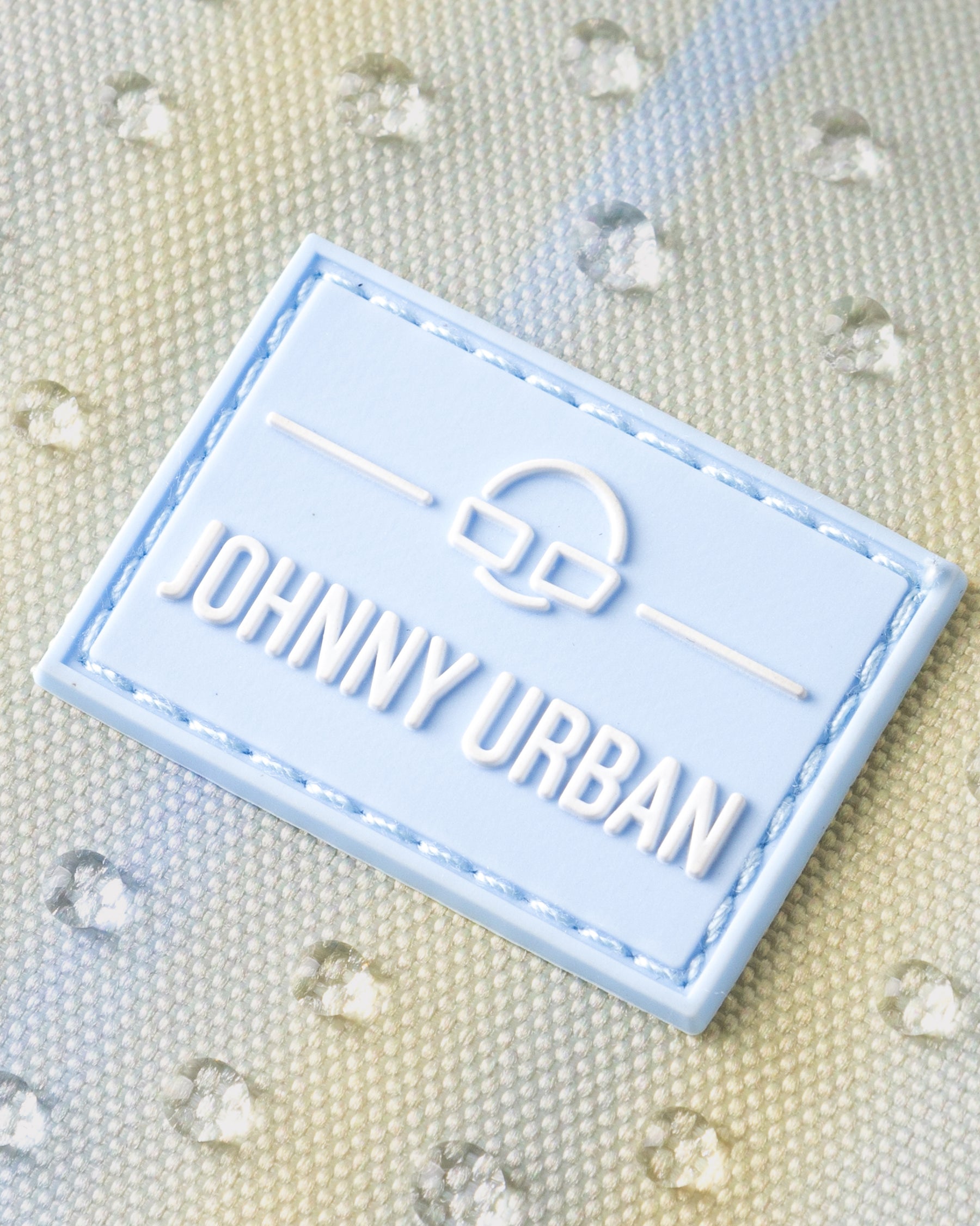 Nahe Aufnahme des wasserabweisenden, sandfarben gestreiften Materials der Bauchtasche 'Erik Small' mit hellblauem 'Johnny Urban'-Label