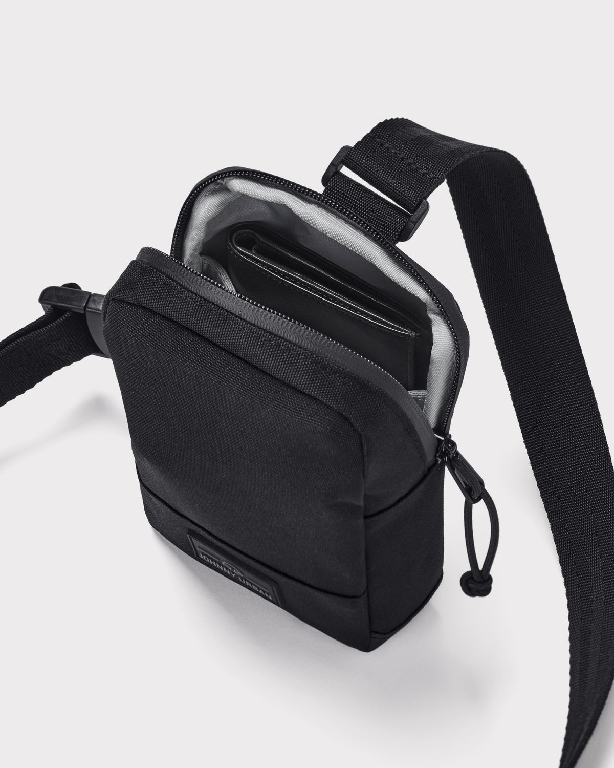 Schwarze Brusttasche 'Arthur' von Johnny Urban mit Reißverschluss geöffnet, darin ein Portemonnaie